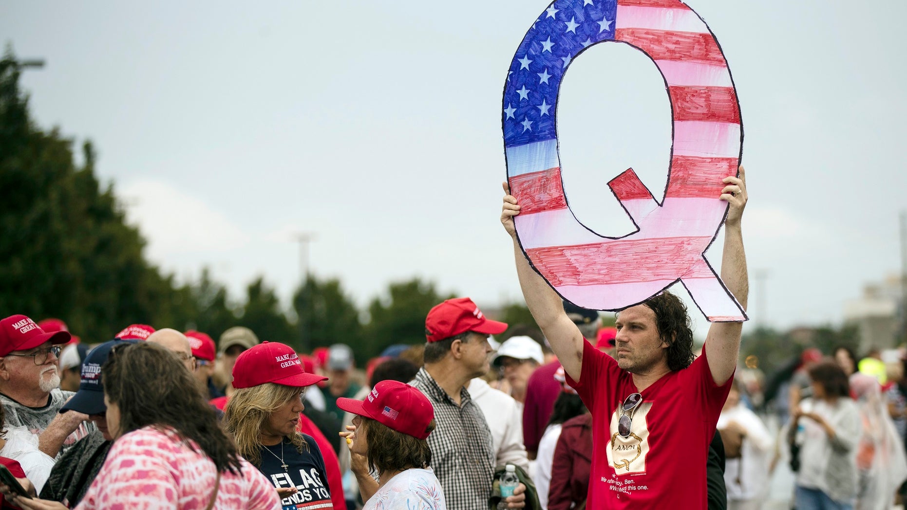 A man holds a 'Q' sign while waiting to enter a Pennsylvania rally with President Trump.
