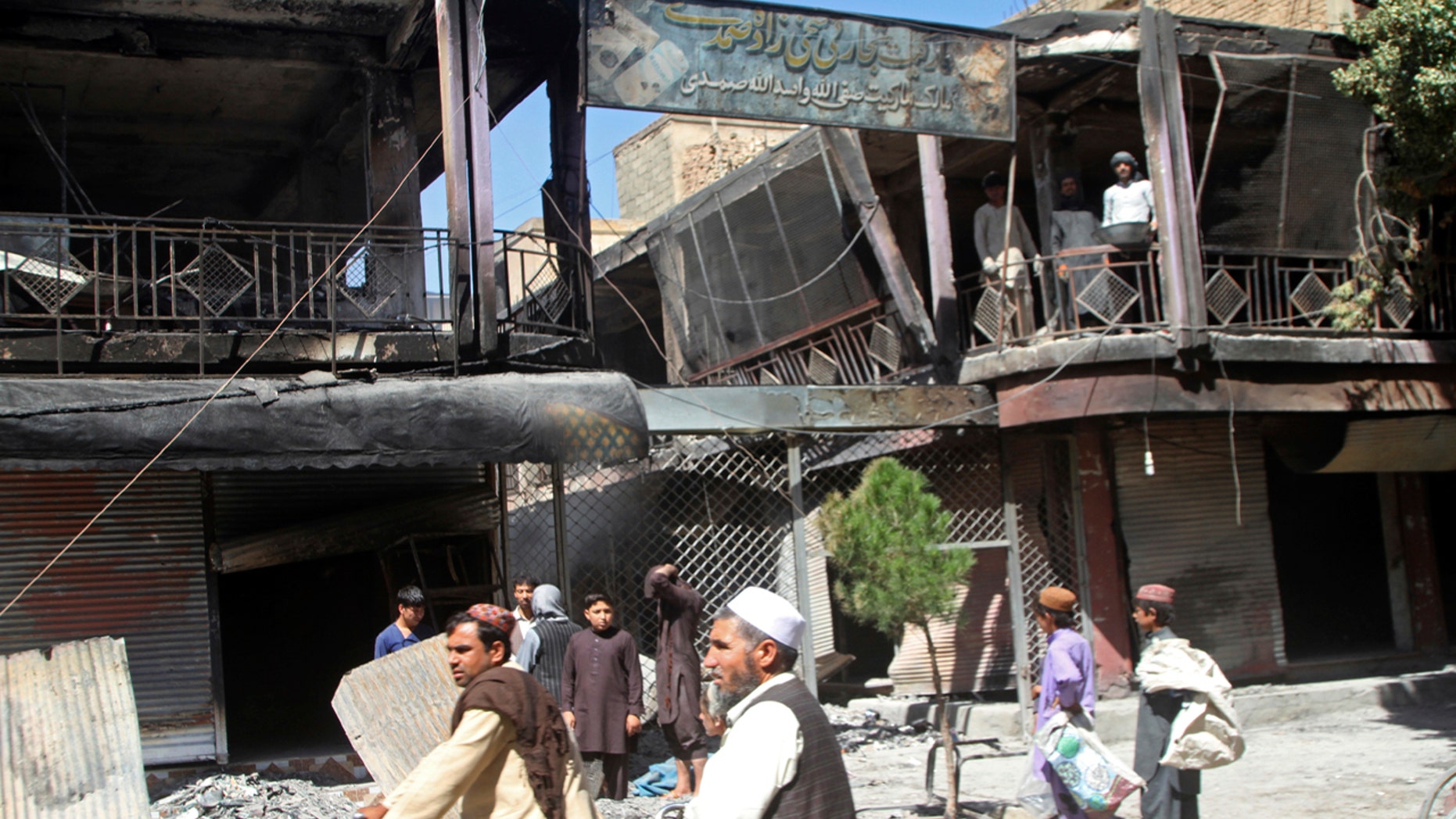 Afghan men stand in front of burned out shops following a Taliban attack in Ghazni, Afghanistan, Wednesday, Aug. 15, 2018.