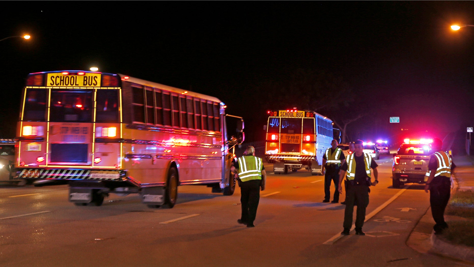 Police officers stand watch as spectators are bussed from a shooting incident at a practice football game between Dwyer and Palm Beach Central High School Friday, Aug. 17, 2018, in Wellington, Fla.