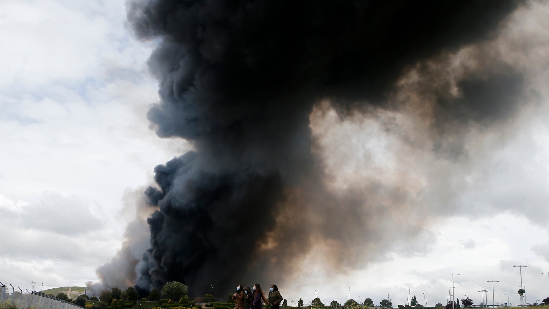 Four women walk with masks in front of billowing black smoke from a huge fire in Sesena, central Spain, Friday, May 13, 2016. A massive fire is raging at a sprawling tire dump in a town near Madrid, sending a spectacular cloud of thick black smoke into the air that's visible for at least 30 kilometers (20 miles). Ten teams of firefighters are trying to put out the blaze at the tire dump in the town of Sesena, still raging more than 10 hours after it started. (AP Photo/Paul White)