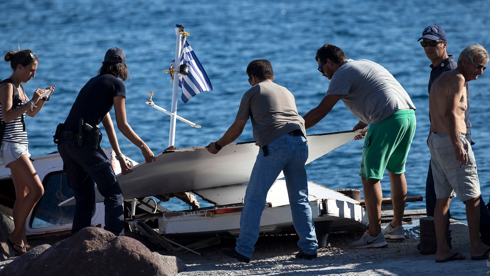 A Coast guard officer and two men move parts of the tourist vessel after the crash.