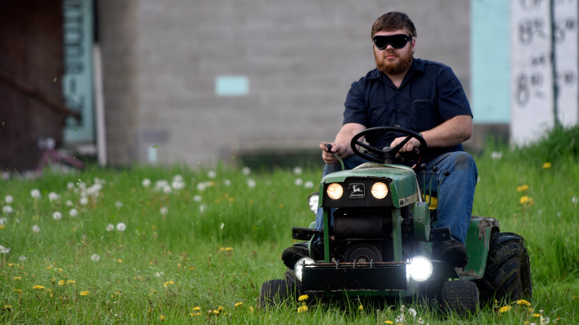 In this photo taken Wednesday May 11, 2016, Detroit Mower Gang member Nick Myer, of Clinton Township, Mich., drives his lawnmower blindfolded during a blindfolded mower contest at Hammerberg Field on Detroit's west side. The volunteers helping to maintain Detroit parks and playgrounds took a crack at mowing grass while blindfolded as part of a friendly competition. (Steve Perez/Detroit News via AP) DETROIT FREE PRESS OUT; HUFFINGTON POST OUT; MANDATORY CREDIT