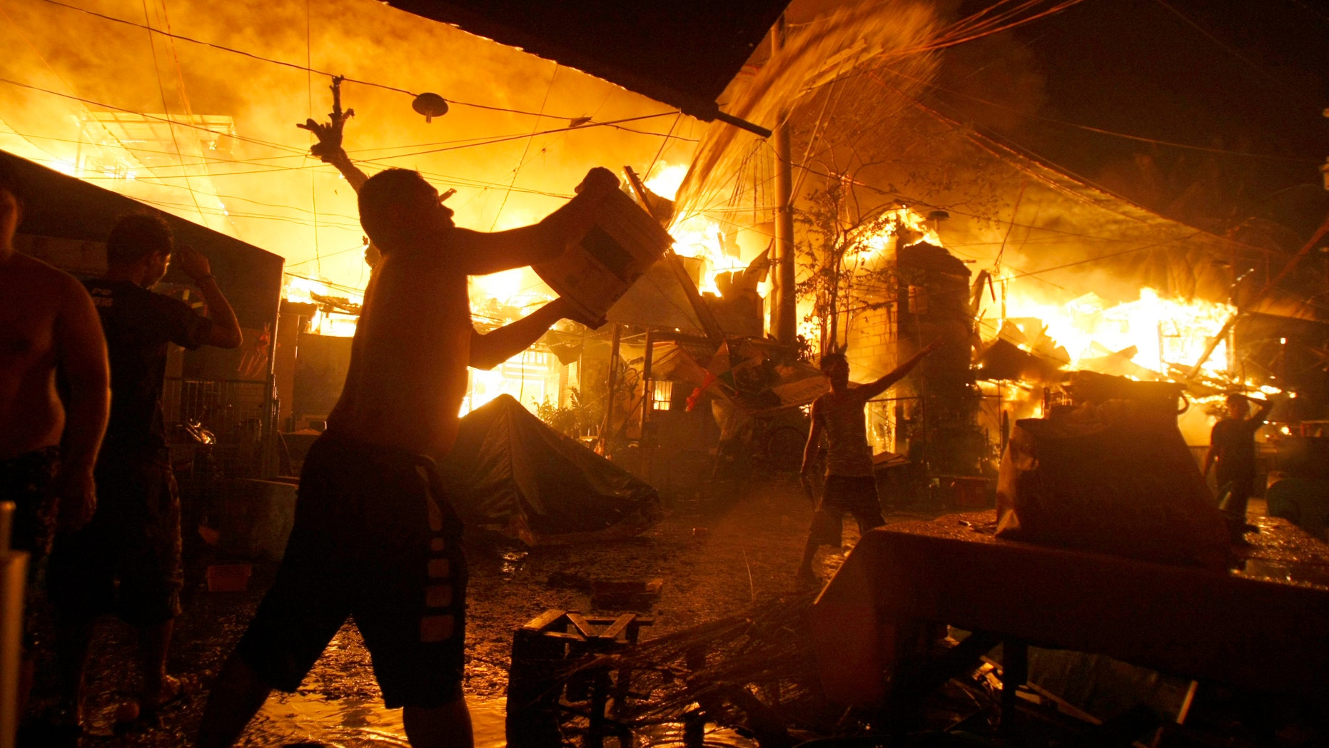 A man throws a bucket of water to help firemen battle a fire that occurred as Filipinos welcome the New Year at a poor Manila district of Tondo Friday, Jan. 1, 2016 in the Philippines. The cause of the fire is still under investigation but a number of fires that occurred in the raucous New Year celebrations in the country are attributed to firecracker explosions. (AP Photo/Linus Escandor II)