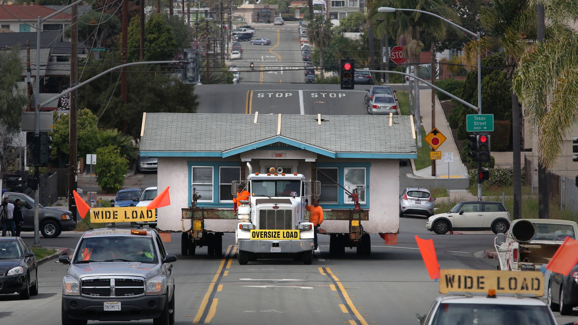 In this photo taken Monday, March 28, 2016, workers oversee the hauling of a small home in Hillcrest, Calif., as it left the plot of land on the corner of Vermont Street and is moving east along Howard Avenue. The home, built in 1925, was being moved to a storage yard in Otay Mesa, Calif., before finally being relocated to a new lot in Chula Vista, Calif. The owner, Anne Wilson, had lived in the 800-square-foot stucco home for 23 years, plans to build a new three-story home on the lot. (Peggy Peattie/The San Diego Union-Tribune via AP) NO SALES; MANDATORY CREDIT