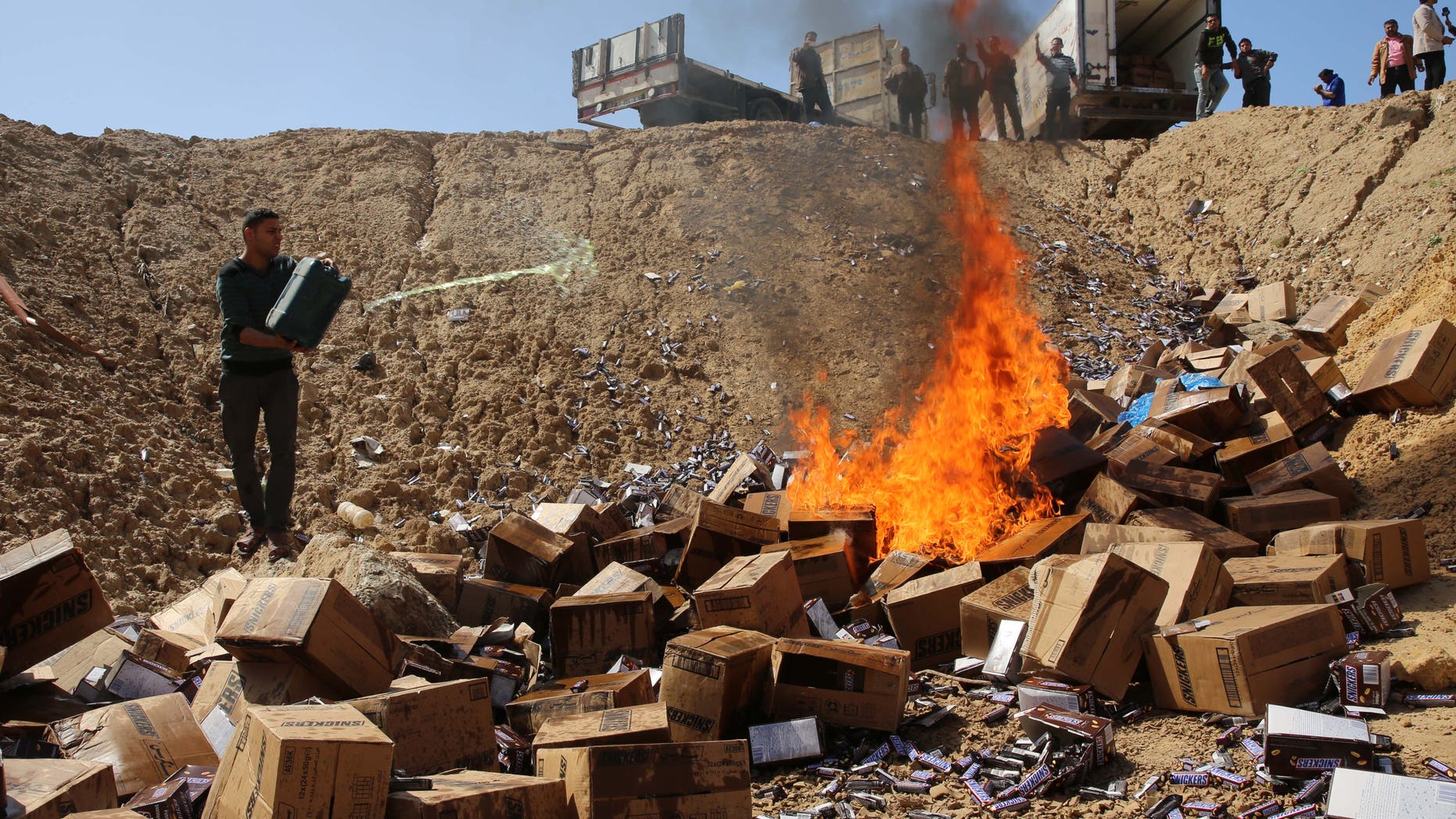 Palestinian worker throws gasoline on buringing boxes of Snickers chocolate on the outskirts of Gaza City, Thursday, March 10, 2016. Hamas authorities in Gaza say they disposed of 15 tons of chocolate in response to a mass recall the manufacturing company issued last month. (AP Photo/Adel Hana)
