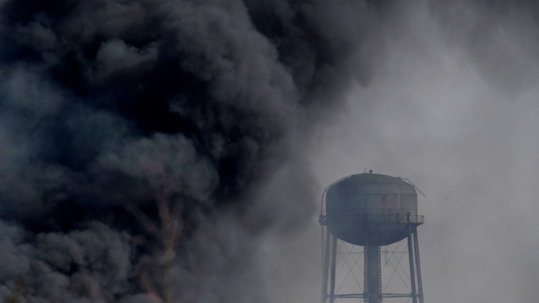 Smoke rises near a water tower at the site of a large warehouse fire a day after flames engulfed the facility, Friday, Feb. 12, 2016, in Hillsborough, N.J. Firefighters have contained the massive fire and officials said the blaze didn't pose an imminent public health threat. Fire officials say plastic pellets were being stored in most of the complex, and environmental officials have been testing air quality. (AP Photo/Julio Cortez)