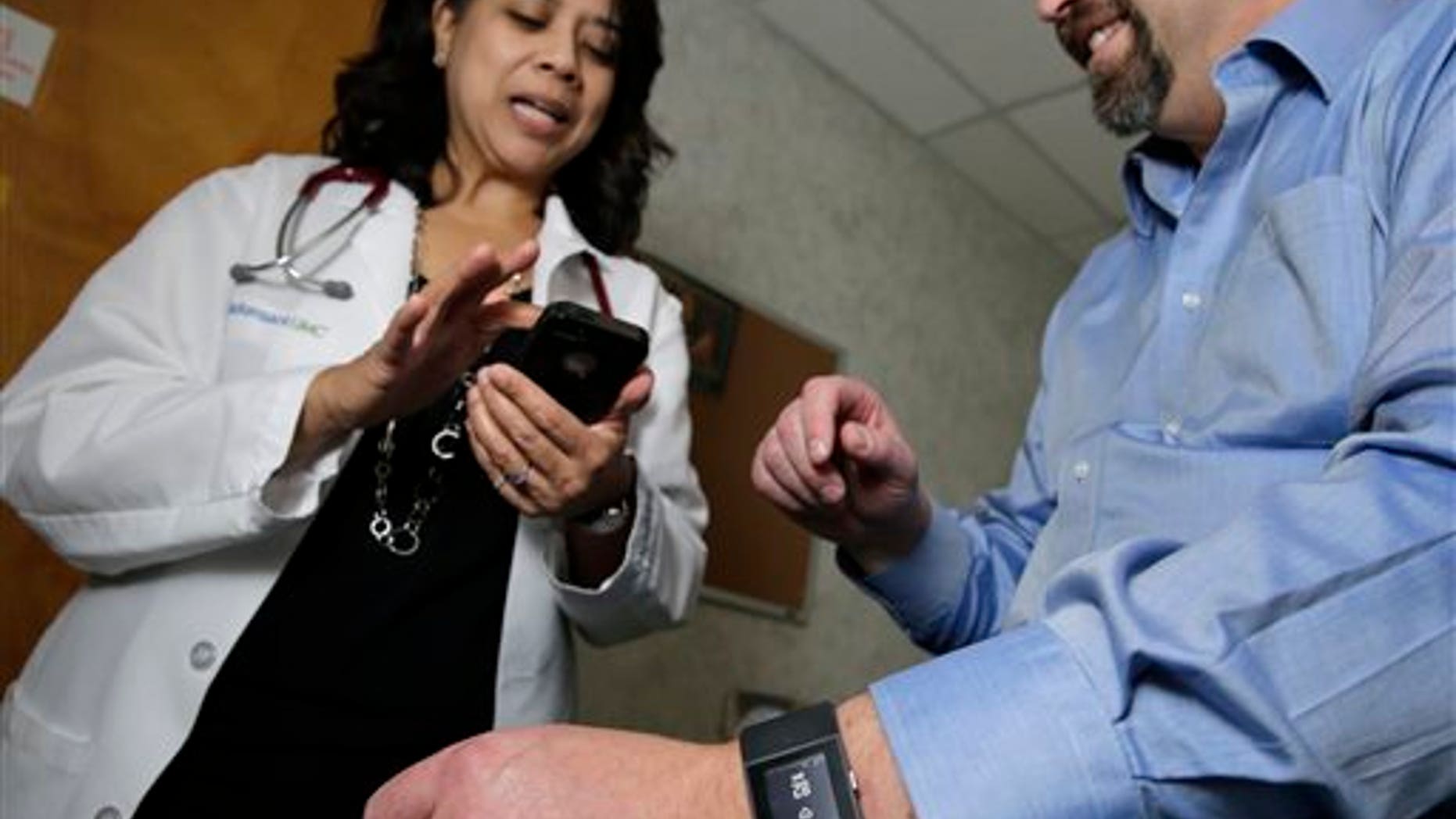 In this Thursday, Feb. 5, 2015 photograph, Hackensack University Medical Center cardiologist Dr. Sarah Timmapuri, left, looks at data on a smart phone that is synchronized to a new Fitbit Surge that is on the wrist of patient Gary Wilhelm, 51, during an examination in Hackensack, N.J. (AP Photo/Mel Evans)