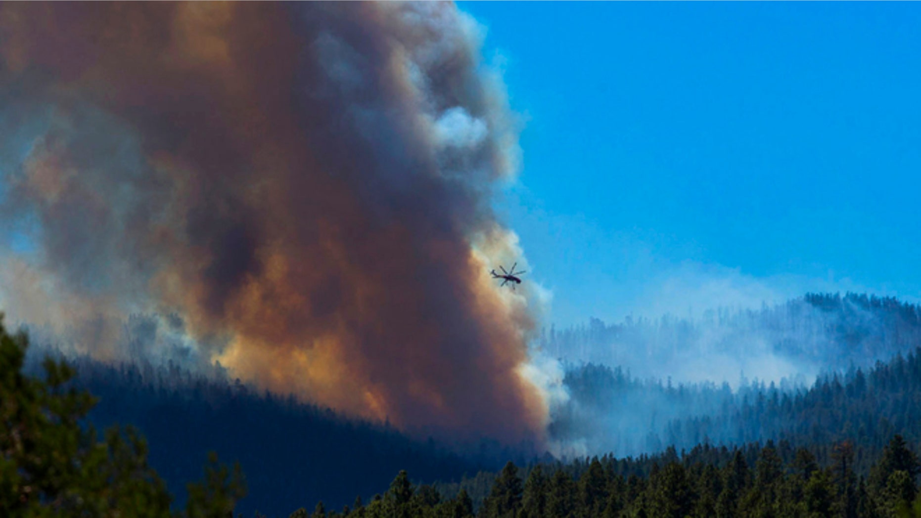 June 27, 2014: A helicopter battles the blaze with lake water as smoke rises from the trees of the San Juan fire near Vernon, Ariz.