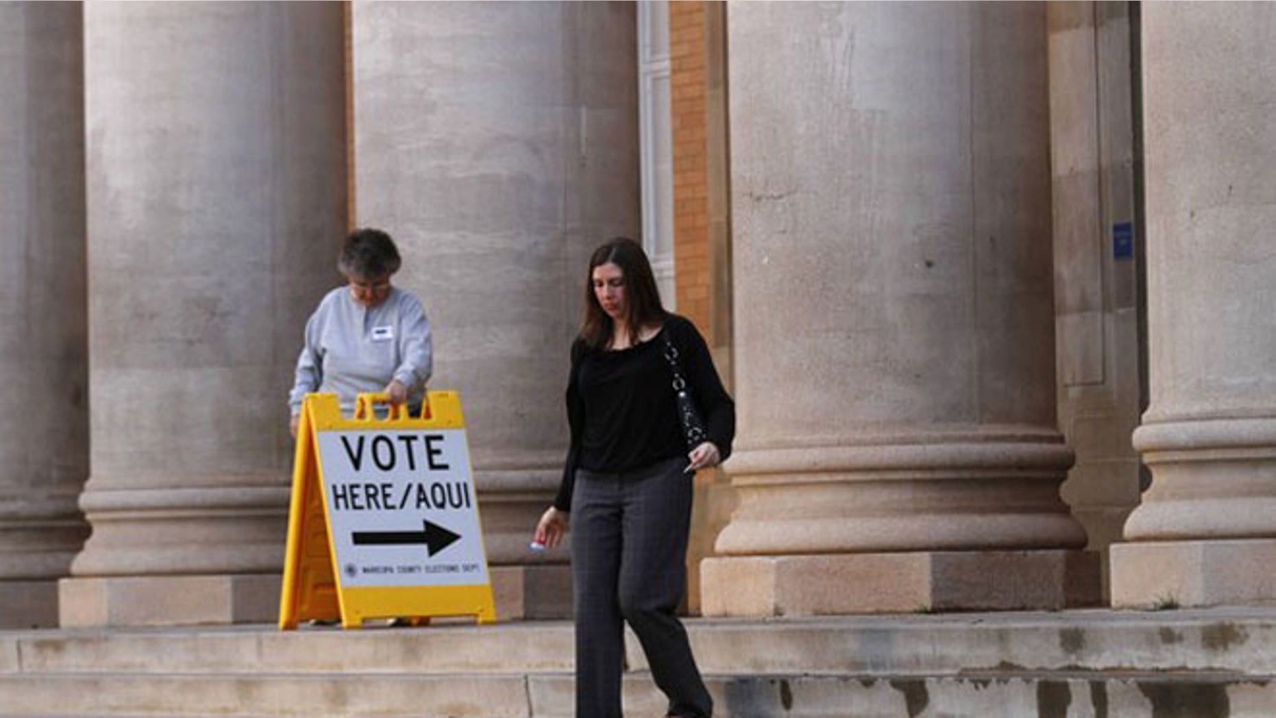 February 28, 2012: Sarah Moran leaves a polling station after voting as election-day volunteer Vicki Groff moves a vote sign at Kenilworth School in Phoenix, Arizona.