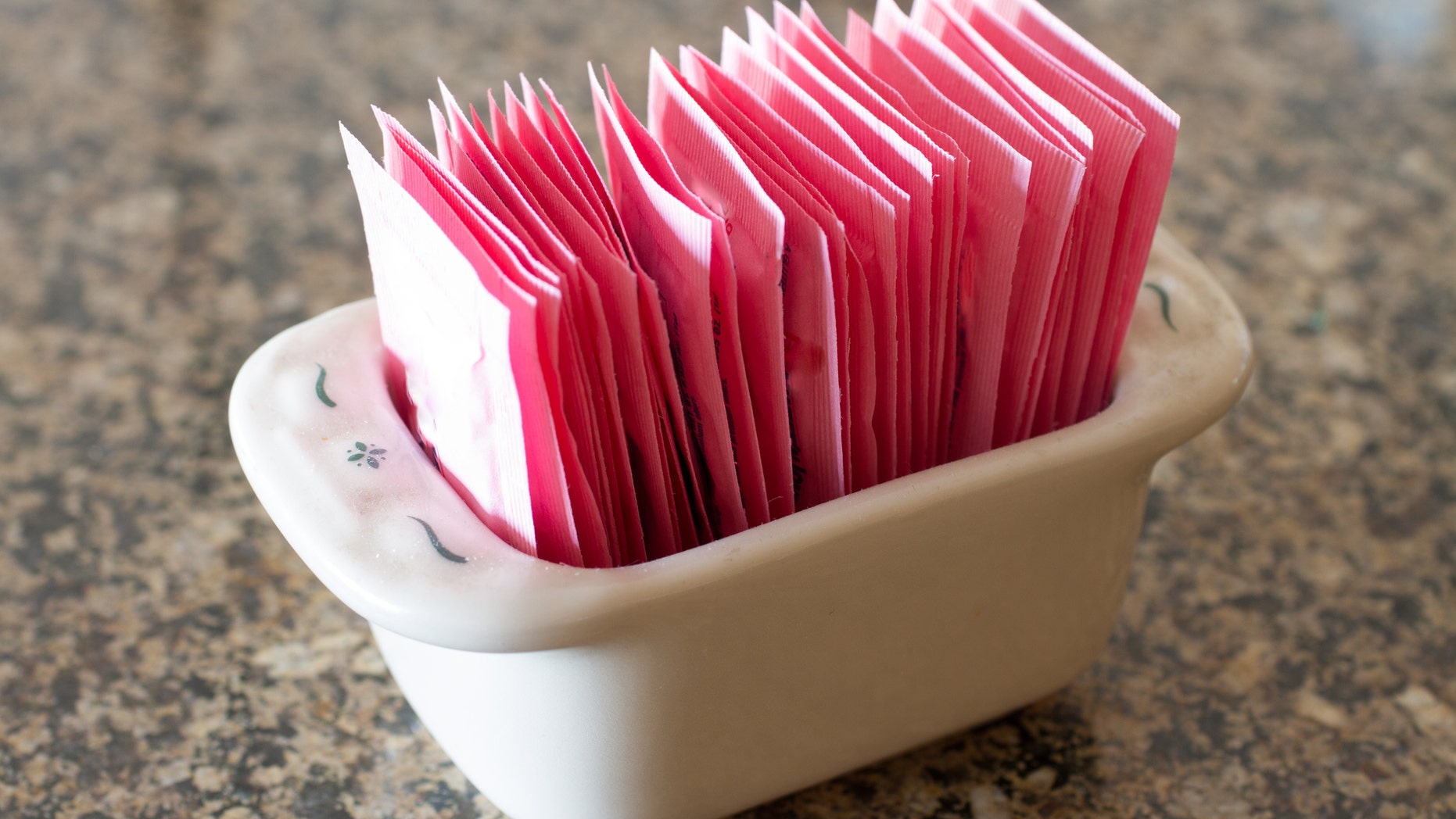 A stoneware container holding packets of artificial sweetener.
