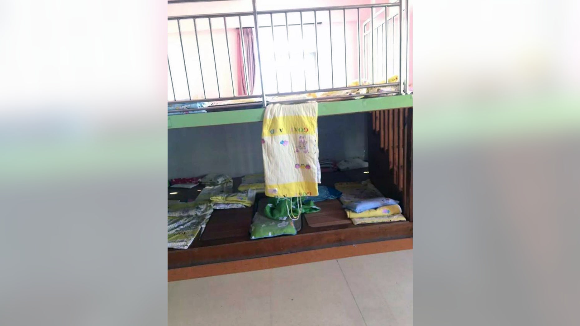 Pic shows: The sleeping platforms in the classroom and the hanging quilt
A young boy has died in a freak nap time accident at his nursery school after ropes on a blanket became tangled around his neck.
The four-year-old surnamed Lin was one of several young pupils who were resting in the Shuangqiao Mingzhu Kindergarten classroom after lunch and is believed to have suffocated by himself.
According to the childâs teacher, the boy was found without breath sounds at 2pm when nap time ended, and he was confirmed dead after being rushed to hospital in Xiamen City, in East Chinaâs Fujian Province.
The nursery school said thin ropes attached to the classroomâs quilts - specially designed to be rolled up and easily carried - had somehow become wrapped around the childâs neck when dangling from above.
The school said the boy, who was sleeping on the lower of two platforms, most likely lost consciousness and later died of asphyxiation shortly after.
Investigators have already ruled out murder and manslaughter from the tragic case, but are now looking into the matter and could charge the teacher and the school principal with negligence.
The teacher claimed to have been too distracted by all the other pupils in class and did not pay special attention to the young victim, whose post-mortem photographs show clear signs of bruising around his neck.
It is unclear whether the nursery school has offered to compensate the Lin family for their tragic loss.
(ends)