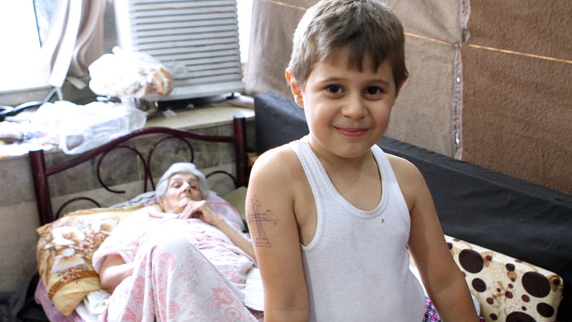 Aws, a 10-year-old Iraqi Christian boy, has spent much of his young life fleeing jihadists. Munira Aziz, 74,pictured behind him, considers herself fortunate to have escaped ISIS. (Benjamin Hall)