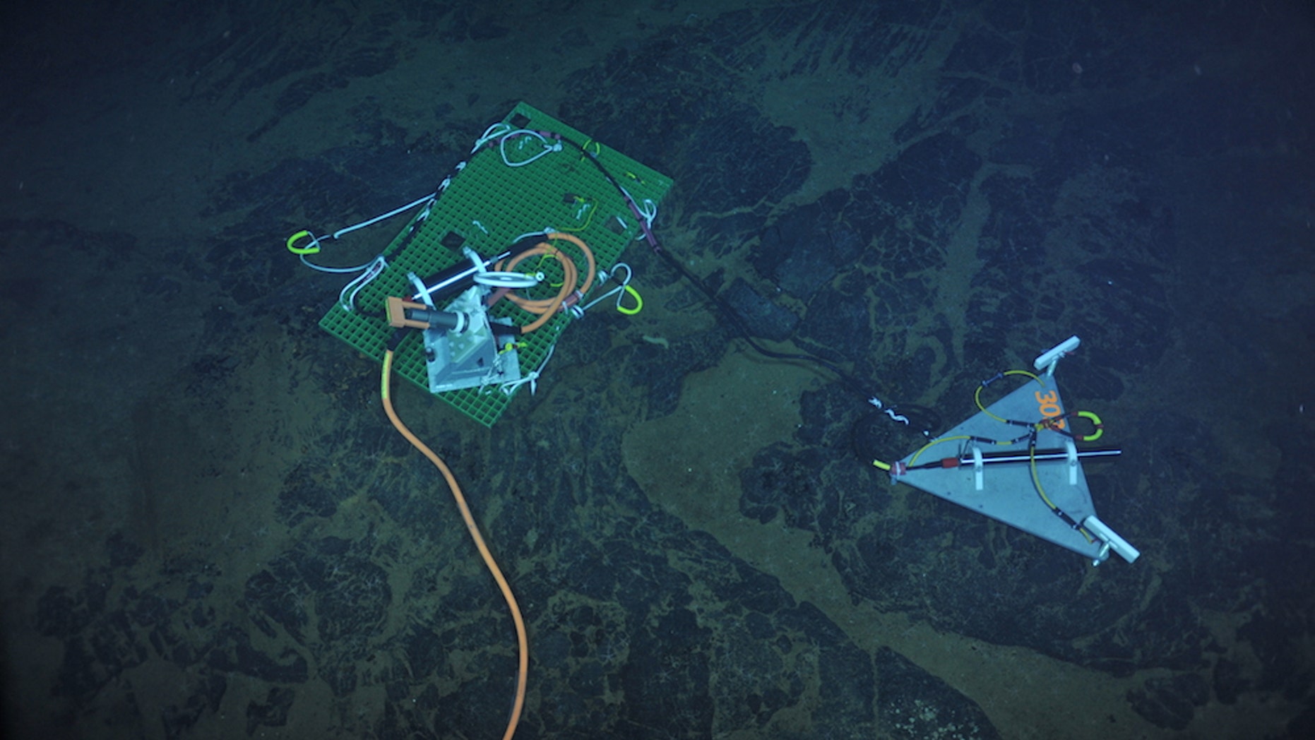 A seismometer (long black cylinder, right) installed in 2013 atop the Axial Seamount. The green plate transmits real-time data to the orange cable and then back to shore as part of the National Science Foundation’s Ocean Observatories Initiative.