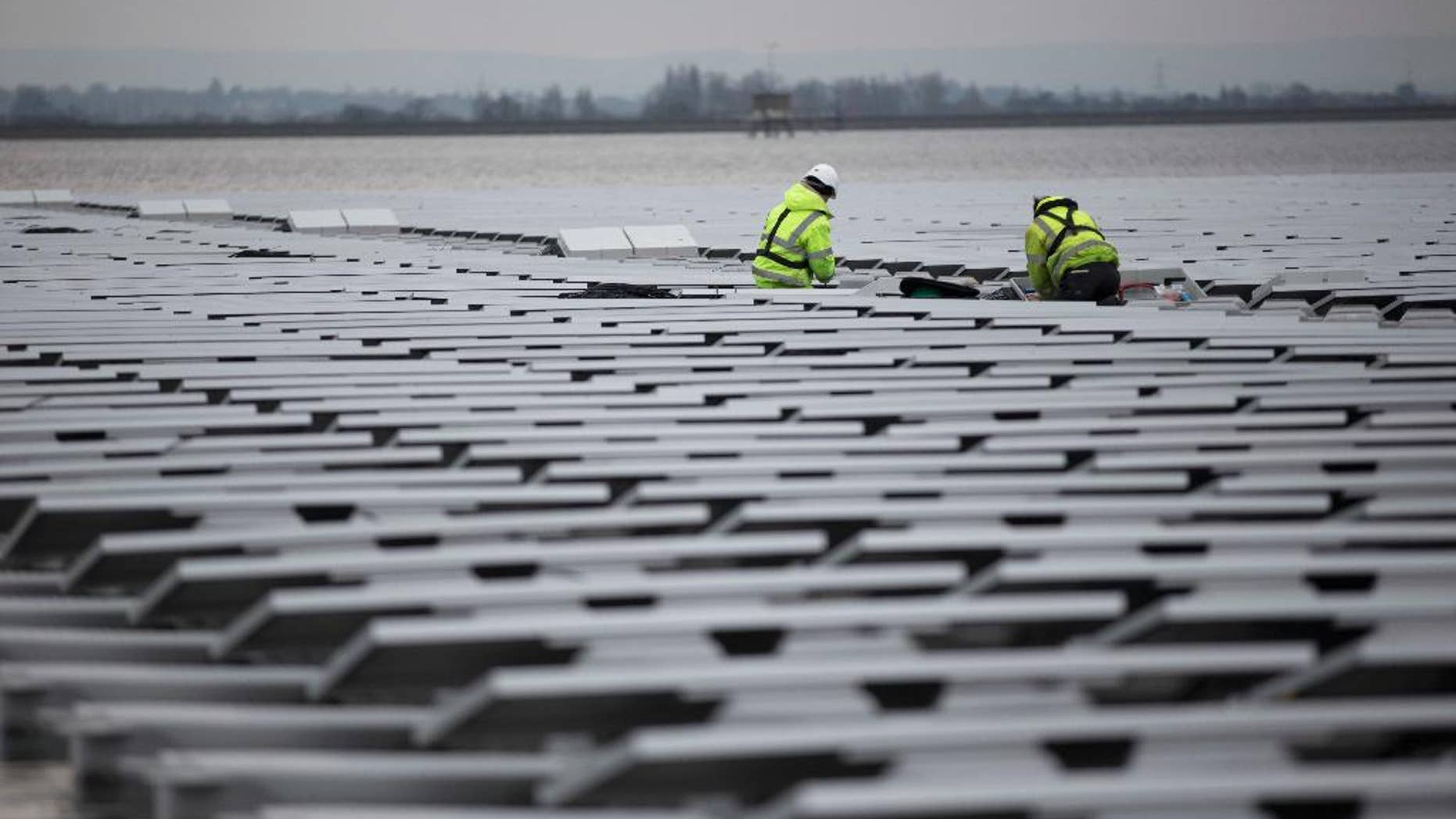 FILE - This is a Monday, March 21, 2016 file photo of contractors continue work on Europe's biggest floating solar panel array as it nears completion on the Queen Elizabeth II Reservoir near Walton-on-Thames in south west London. Data published Tuesday June 21, 2016 by the European Environment Agency show that Britain’s greenhouse gas emissions fell by 34.3 percent in 1990-2014, the biggest percentage drop in the EU except for eastern countries whose emissions fell sharply when communist-era heavy industries collapsed. (AP Photo/Matt Dunham, File)