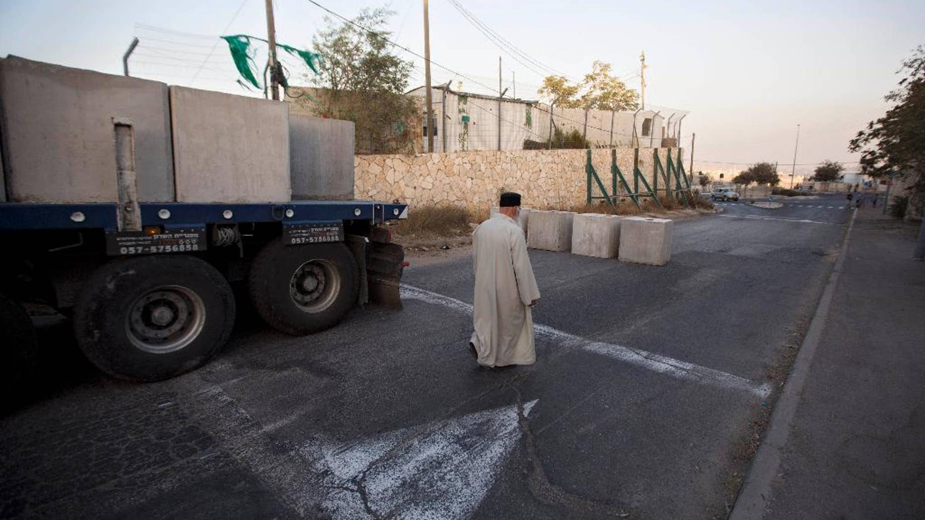 A Palestinian man walks past newly placed concrete blocks on the road at the entrance to the east Jerusalem neighborhood of Jabal Mukaber, Wednesday, Oct. 14, 2015. The Israeli military began deploying hundreds of troops in cities across the country on Wednesday to assist police forces in countering a wave of deadly Palestinian shooting and stabbing attacks that have created panic across the country. (AP Photo/Sebastian Scheiner)