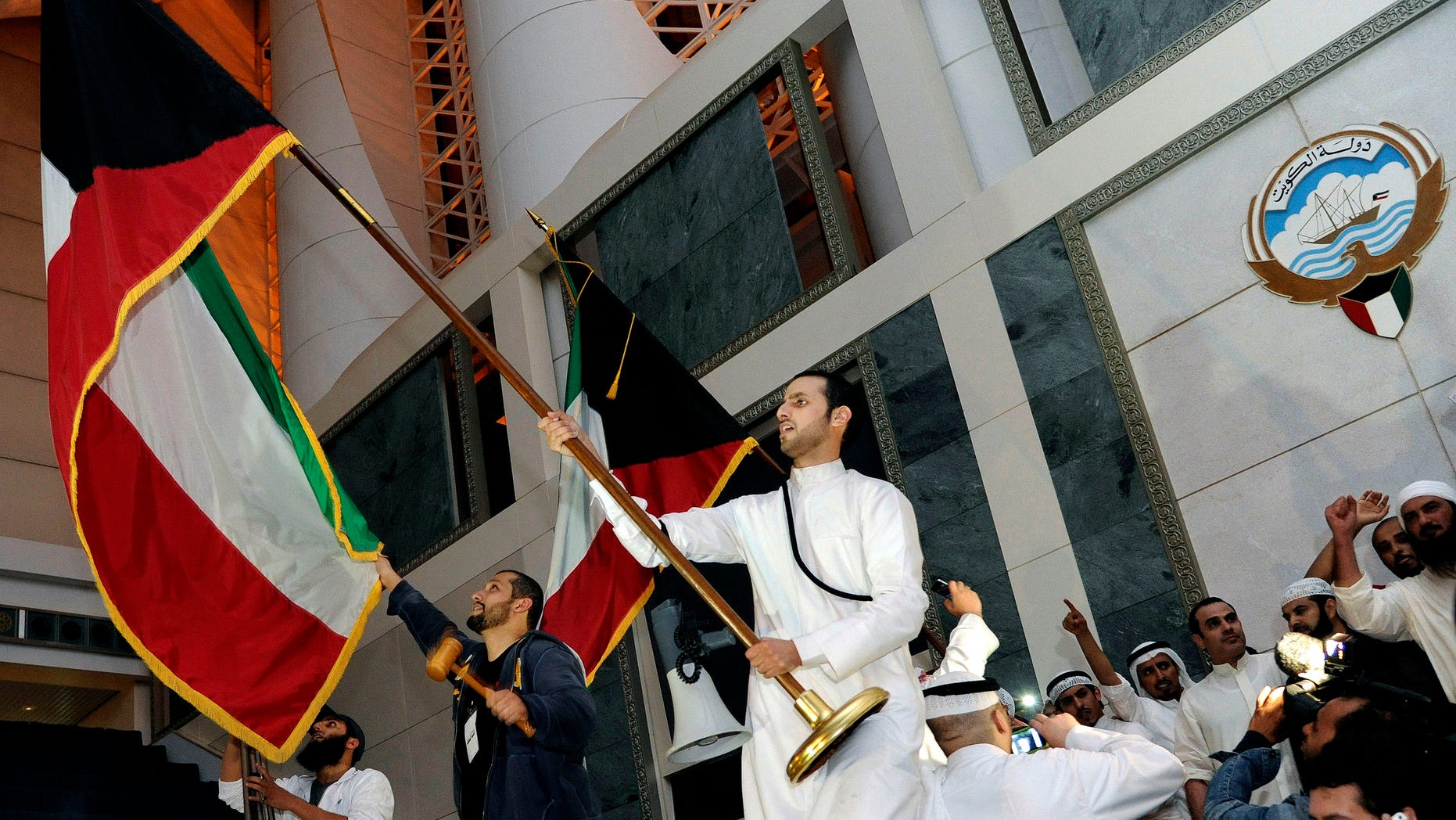 FILE - In this Wednesday, Nov. 16, 2011 file photo, Kuwaiti men wave flags after storming Kuwait's parliament building as hundreds of others protest outside the building, in Kuwait City. A lawyer defending 70 Kuwaiti opposition members on trial in connection with the 2011 storming of the oil-rich Gulf nation’s parliament says they have been found not guilty. (AP Photo/Nasser Waggi, File)
