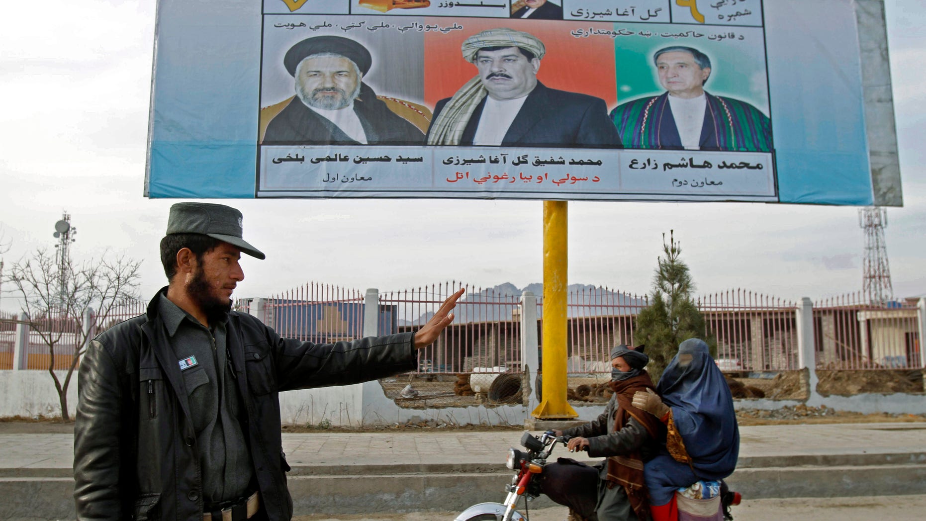 An Afghan policeman stands guard at a temporary checkpoint as a man on a motorcycle rides past an election poster of presidential candidate, Mohammad Shafiq Gul Agha Sherzai, center, in Kandahar, south of Kabul, Afghanistan, Sunday, Feb. 9, 2014. (AP Photo/Allauddin Khan)