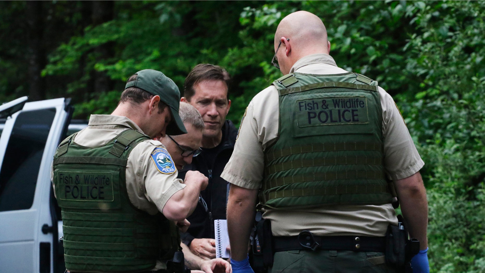 Washington State Fish and Wildlife Police confer with an individual from the King County Medical Examiner's and a King County Sheriff's deputy on a remote gravel road above Snoqualmie, WA., following a fatal cougar attack. Saturday May 19, 2018.