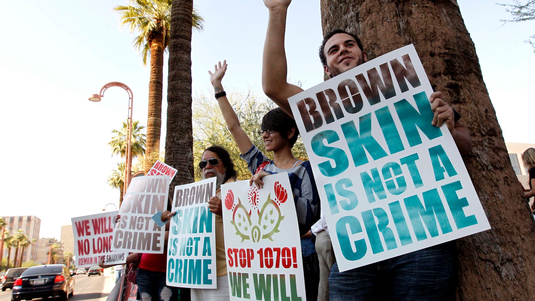 Laurent Taillefer, right, and Andrea Begay, second from right, both of Phoenix, wave at cars as they honk their horns driving by as the two join immigration rights protesters as they gather after the United States Supreme Court decision regarding Arizona's controversial immigration law, SB1070, at the local U.S. Immigration and Customs Enforcement offices Monday, June 25, 2012, in Phoenix. The Supreme Court struck down key provisions of Arizonaâs crackdown on immigrants Monday but said a much-debated portion on checking suspectsâ status could go forward. (AP Photo/Ross D. Franklin)