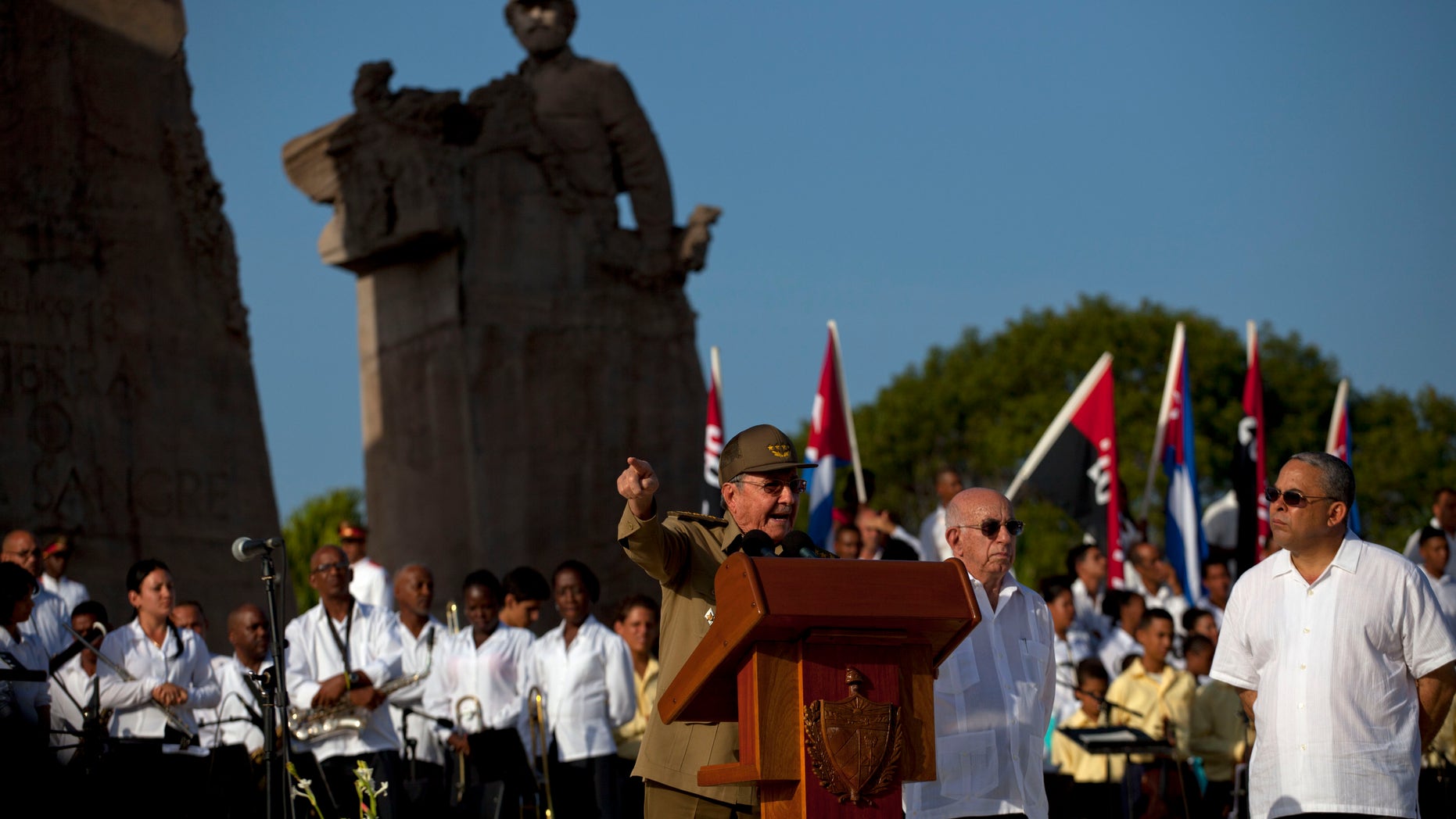 Cuba's President Raul Castro speaks at a podium as Vice President Jose Ramon Machado, second from right, stands by during celebrations marking Revolution Day in Guantanamo, Cuba, Thursday, July 26, 2012. Cuba marks the 59th anniversary of the July 26, 1953 rebel attack led by Fidel and Raul Castro on the Moncada military barracks. The attack is considered the beginning of the revolution that culminated with dictator Fulgencio Batista's ouster. (AP Photo/Ramon Espinosa)