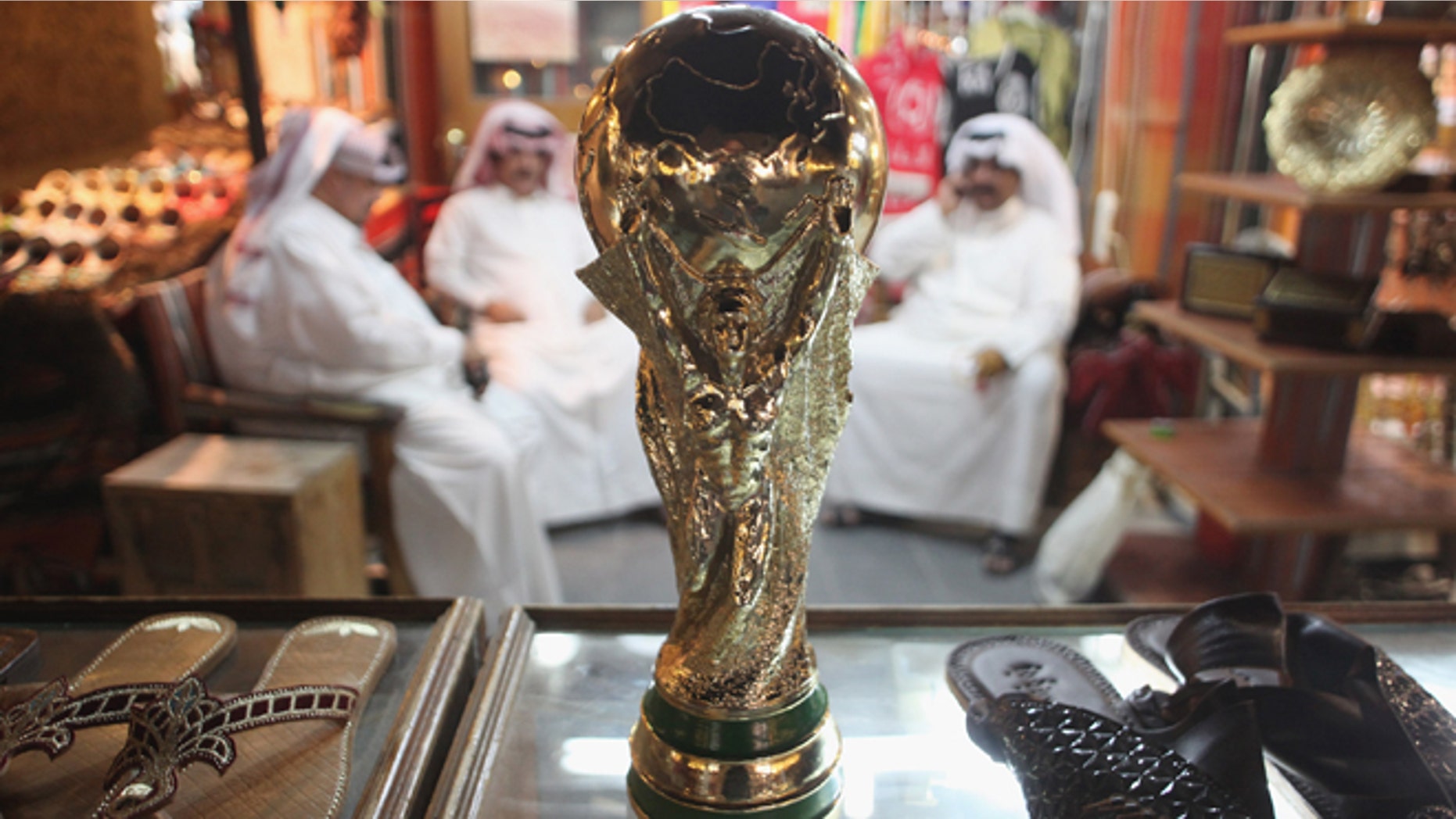 DOHA, QATAR - OCTOBER 24: Arab men sit at a shoemaker's stall with a replica of the FIFA World Cup trophy in the Souq Waqif traditional market on October 24, 2011 in Doha, Qatar. Qatar will host the 2022 FIFA World Cup football competition and is slated to tackle a variety of infrastructure projects, including the construction of new stadiums. (Photo by Sean Gallup/Getty Images)