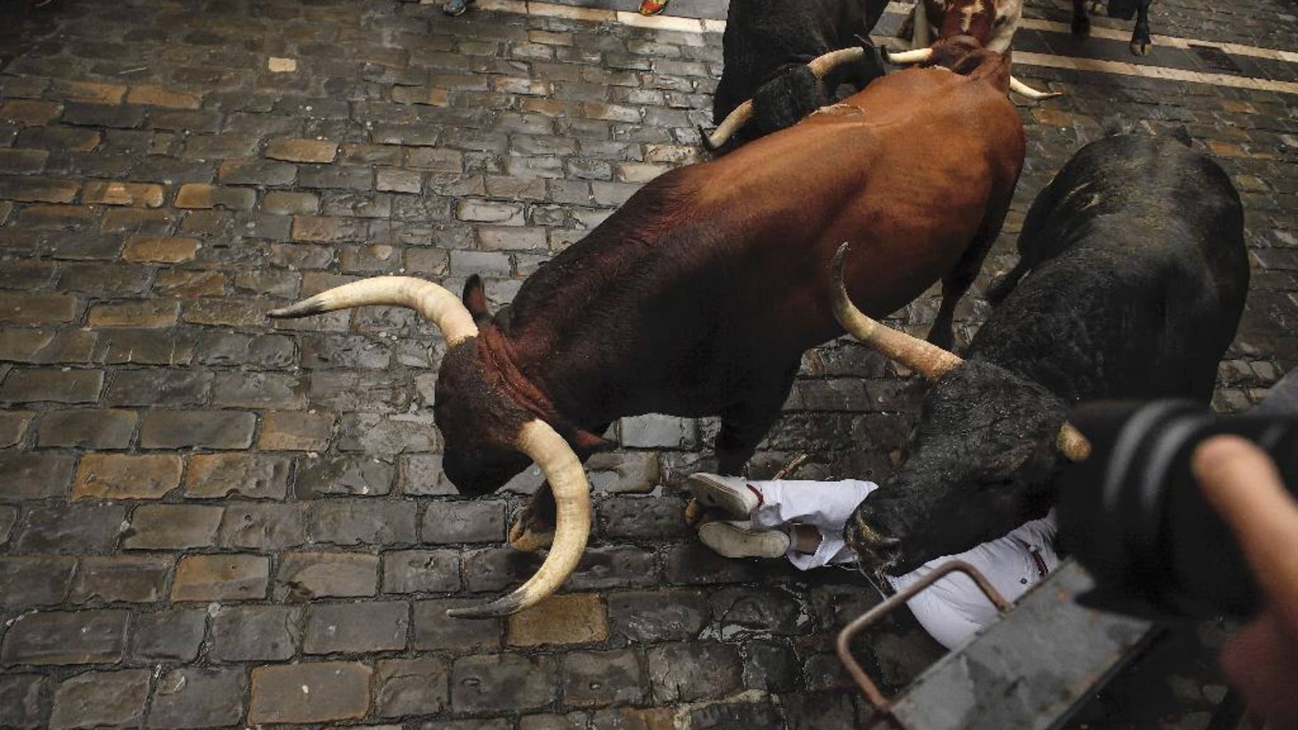 A reveler falls close to a Nunez del Cubillo's fighting bulls on the Estafeta corner during the seventh running of the bulls at the San Fermin Festival, in Pamplona, northern Spain, Wednesday, July 13, 2016. An American was gored in the left leg and taken to a city hospital, spokesman said, and four other runners were hospitalized for contusions. Revelers from around the world flock to Pamplona every year to take part in the eight days of the running of the bulls. (AP Photo/Alvaro Barrientos)