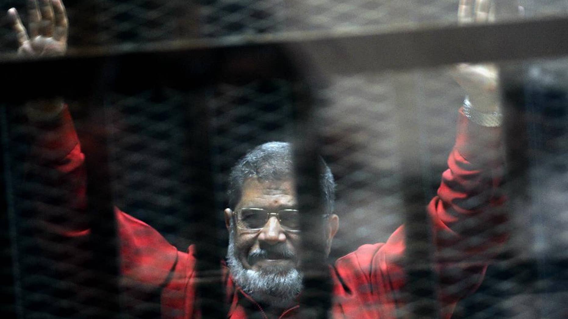 FILE - In this June 21, 2015 file photo, former Egyptian President Mohammed Morsi, wearing a red jumpsuit that designates he has been sentenced to death, raises his hands inside a defendants cage in a makeshift courtroom at the national police academy, in an eastern suburb of Cairo, Egypt. An Egyptian court struck down on Tuesday, Nov. 22, 2016 a life sentence and ordered the retrial of ousted Islamist President Mohammed Morsi on charges of conspiring with foreign militant groups, including the Palestinian Hamas. The decision comes nearly 17 months after the initial sentence against Morsi, who hails from the now-banned Muslim Brotherhood. Along with Morsi's life sentence, those of 16 others, including the group's spiritual leader Mohammed Badei, were thrown out. (AP Photo/Ahmed Omar, File)