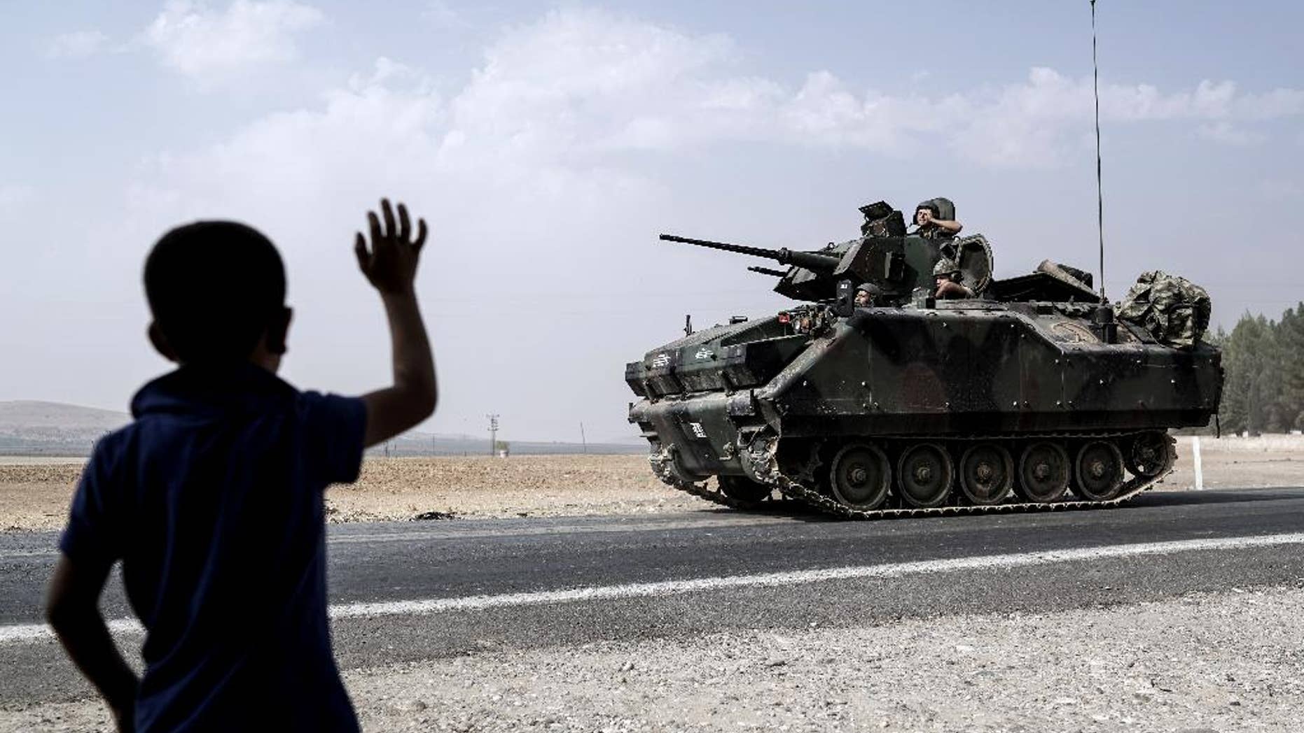A child waves toward Turkish troops heading to the Syrian border, in Karkamis, Turkey, Friday, Aug. 26, 2016. Turkey's state-run Anadolu news agency said late Thursday Turkish artillery have shelled a group of Syrian Kurdish militia fighters in the north of the town of Mambij after they allegedly ignored warnings to retreat. (AP Photo/Halit Onur Sandal)