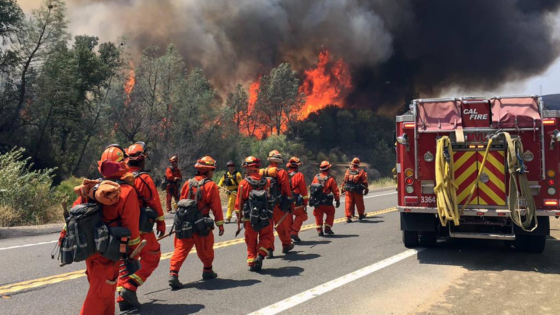Fire crews walk on U.S. Highway 20 as a fire approaches near Clearlake, Calif., Monday, Aug. 3, 2015. Cooler weather helped crews build a buffer Monday between a raging Northern California wildfire and some of the thousands of homes it threatened as it tore through drought-withered brush that hadn't burned in years. (AP Photo/Terry Chea)