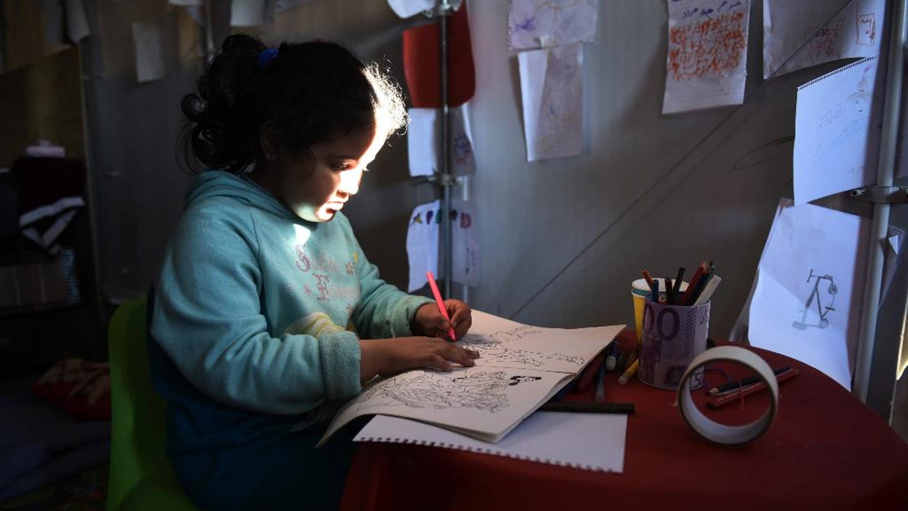 A Syrian girl draws at a refugee camp near the northern Greek village of Idomeni near to southern Macedonia, Monday, Nov. 9, 2015. Migrants are facing long waits to cross Greece's border with Macedonia after a four-day ferry strike ended and eased a bottleneck on the country's eastern Aegean islands, where the vast majority of people arrive from nearby Turkey. (AP Photo/Giannis Papanikos)