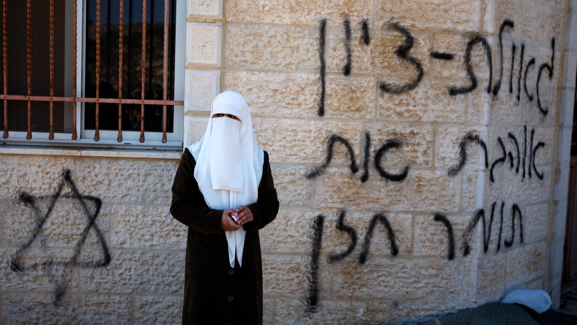 A Palestinian woman stands next to a vandalized mosque in the West Bank village of Burka, near Ramallah, Thursday, Oct. 10, 2013. The Hebrew graffiti reads, "Redemption of Zion, I love Tomer Hazan." Hazan was an Israeli soldier killed by a Palestinian in a West Bank village in September 2013. Palestinian residents of the village said that masked Jewish settlers torched three cars and defaced a mosque during an overnight attack. (AP Photo/Majdi Mohammed)