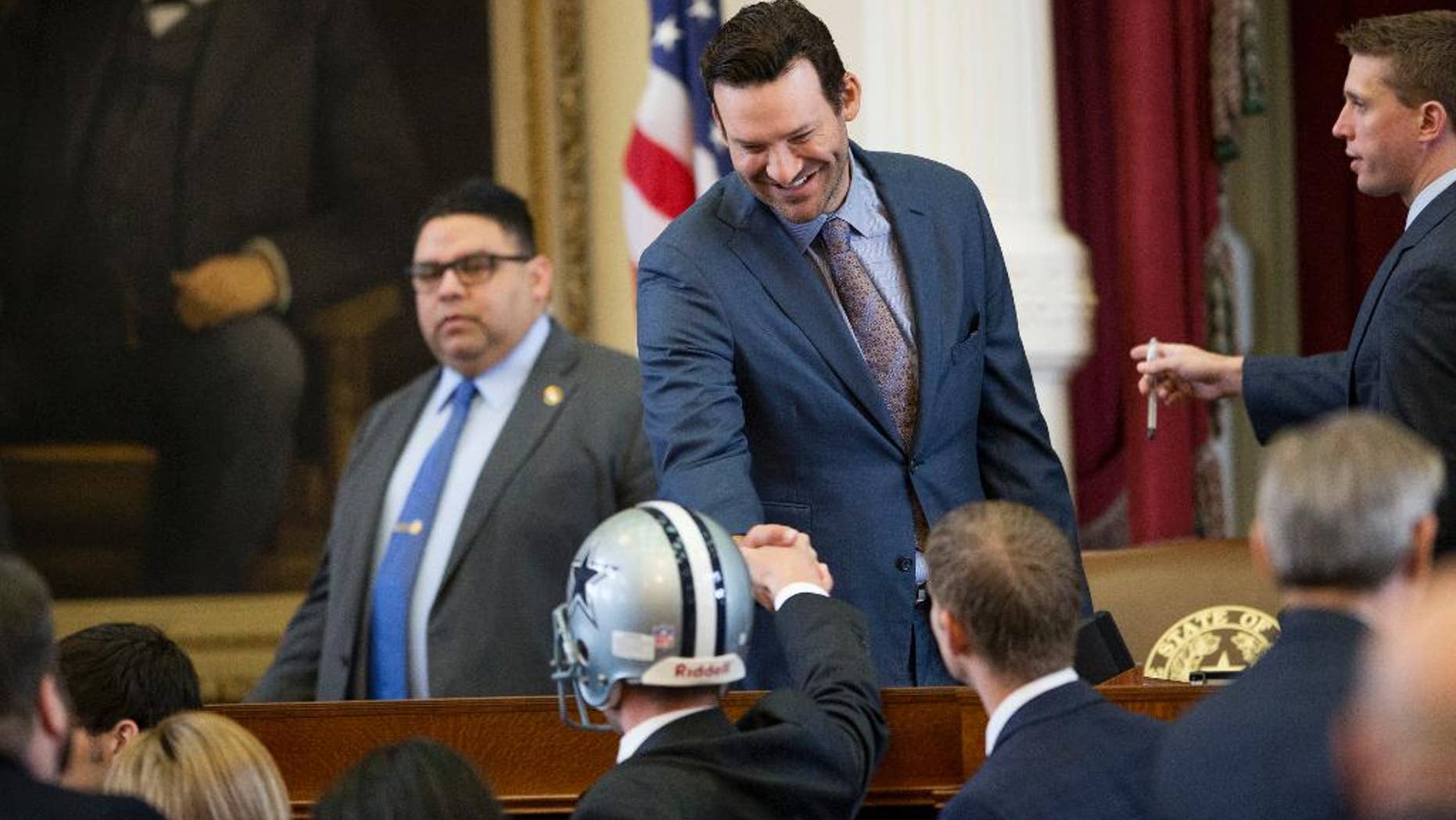 State Rep. Jeff Leach, R-Plano, wearing a football helmet, shakes hands with former Dallas Cowboys quarterback Tony Romo, who was honored in the House Chamber at the Capitol in Austin, Texas, on Wednesday May 3, 2017. (Jay Janner/Austin American-Statesman via AP)