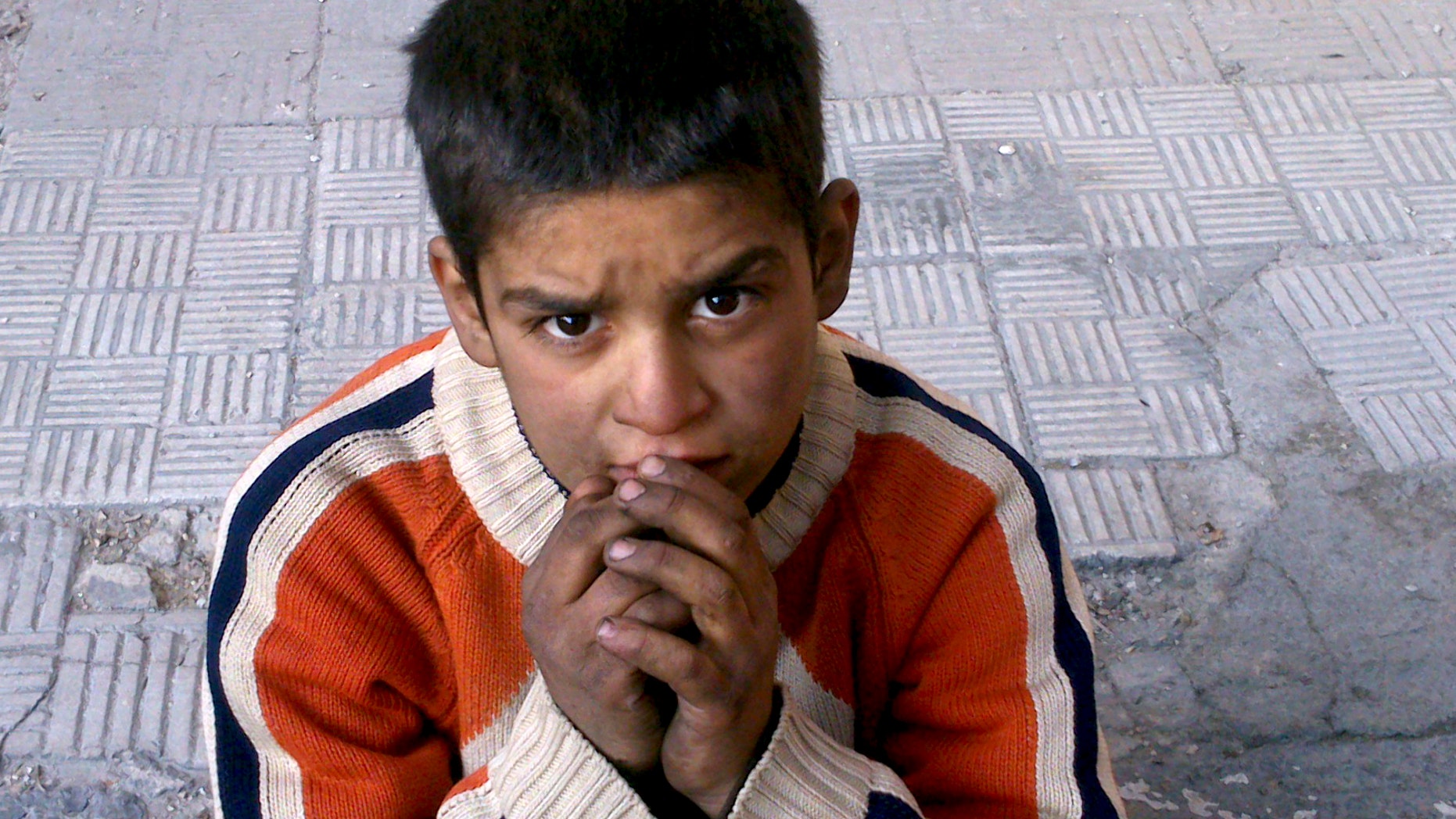 FILE - This Monday, Jan. 6, 2014 activist file photo provided by the group Palestinians of Syria, shows a child sitting on a broken sidewalk after hearing that Syrian authorities would allow civilians to leave in the Palestinian neighborhood of Yarmouk in Damascus, Syria. The chief of the United Nations relief agency supporting Palestinian refugees, Filippo Grandi, said Tuesday he is "deeply disturbed and shaken" by the despair and destruction he'd seen in the besieged Yarmouk refugee camp in the Syrian capital. Many need food and medical treatment immediately, Grandi said in a statement released Tuesday. (AP Photo/Palestinians of Syria, File)