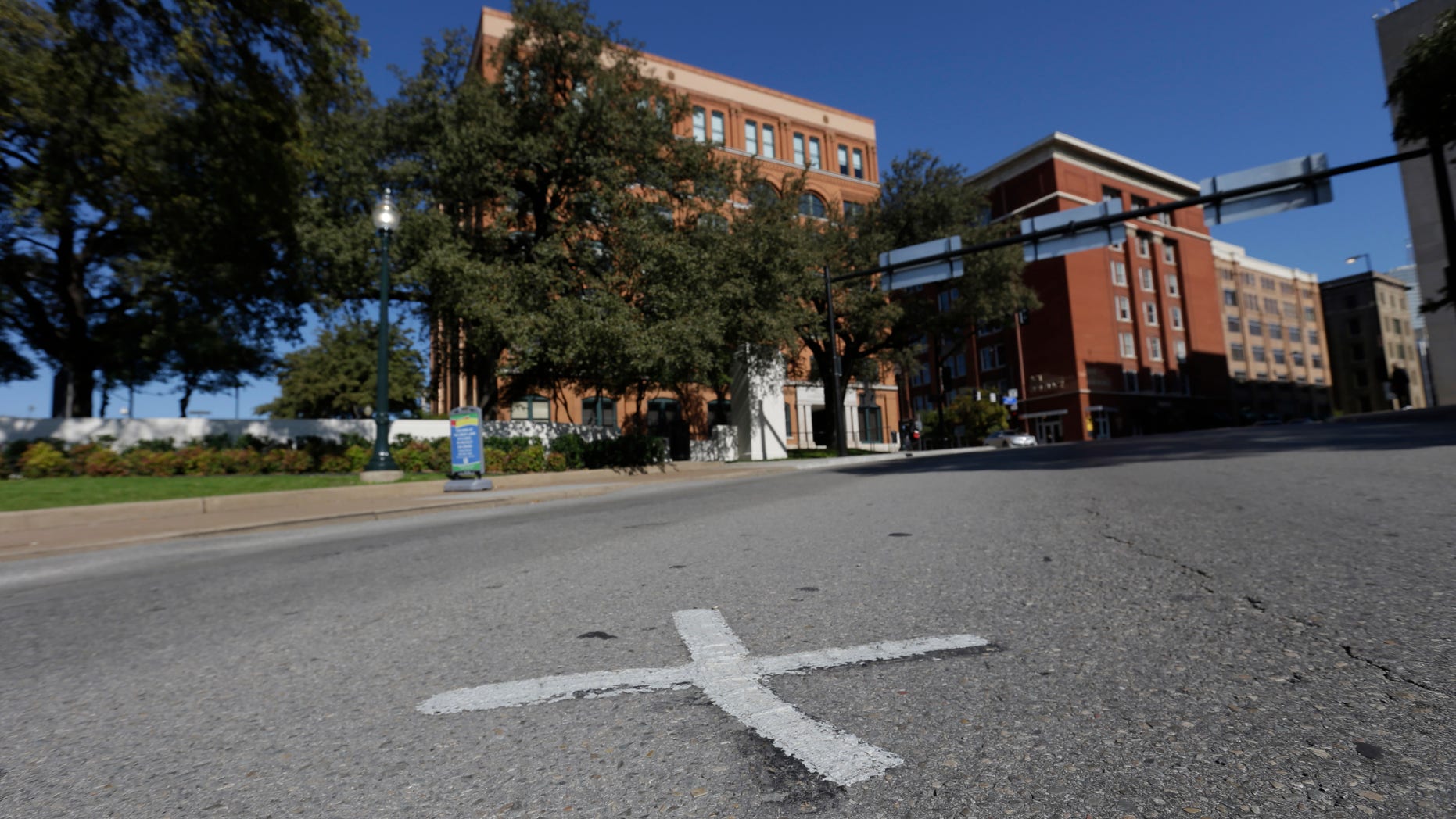 FILE- In this Nov. 12, 2013 file photo, an X marks the spot on Elm Street where the first bullet hit President John F. Kennedy on Nov. 22, 1963 near the former Texas School Book Depository, now known as the Sixth Floor Museum, background, on Dealey Plaza in Dallas. The Xs on the street are gone. The disappearance of the marks come as the city on Friday is set to mark the 50th anniversary of the assassination of John F. Kennedy with a solemn ceremony in Dealey Plaza. (AP Photo/LM Otero, File)