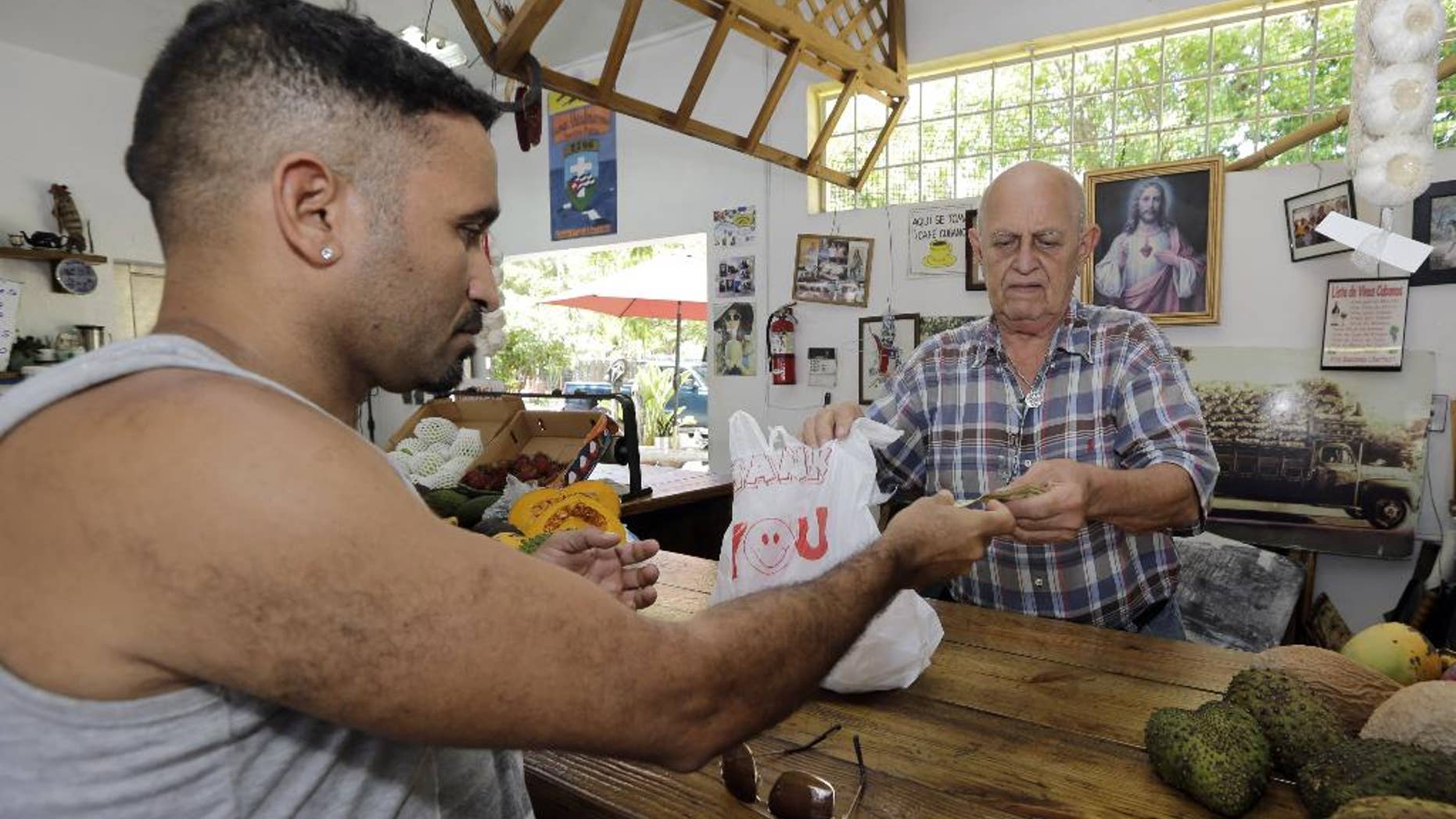 In this June 9, 2015, photo, shopper Miguel Ramirez, left, pays Angel Hernandez for his merchandise at a local fruit store in the Little Havana area of Miami. The University of Michigan issues its monthly index of consumer sentiment for July on Friday, July 31, 2015. (AP Photo/Alan Diaz)