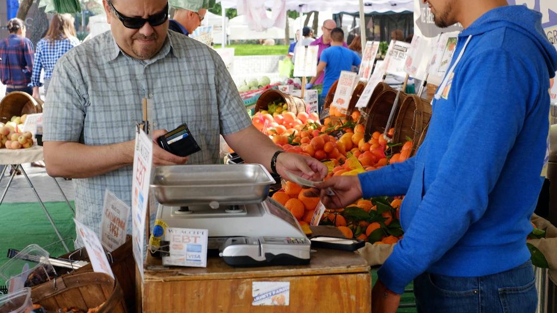 FILE - In this Friday, Feb. 6, 2015 file photo, a shopper pays for his produce at a farmers market in downtown Los Angeles. The Commerce Department releases its April report on consumer spending, which accounts for 70 percent of economic activity, on Monday, June 1, 2015. (AP Photo/Richard Vogel, File)