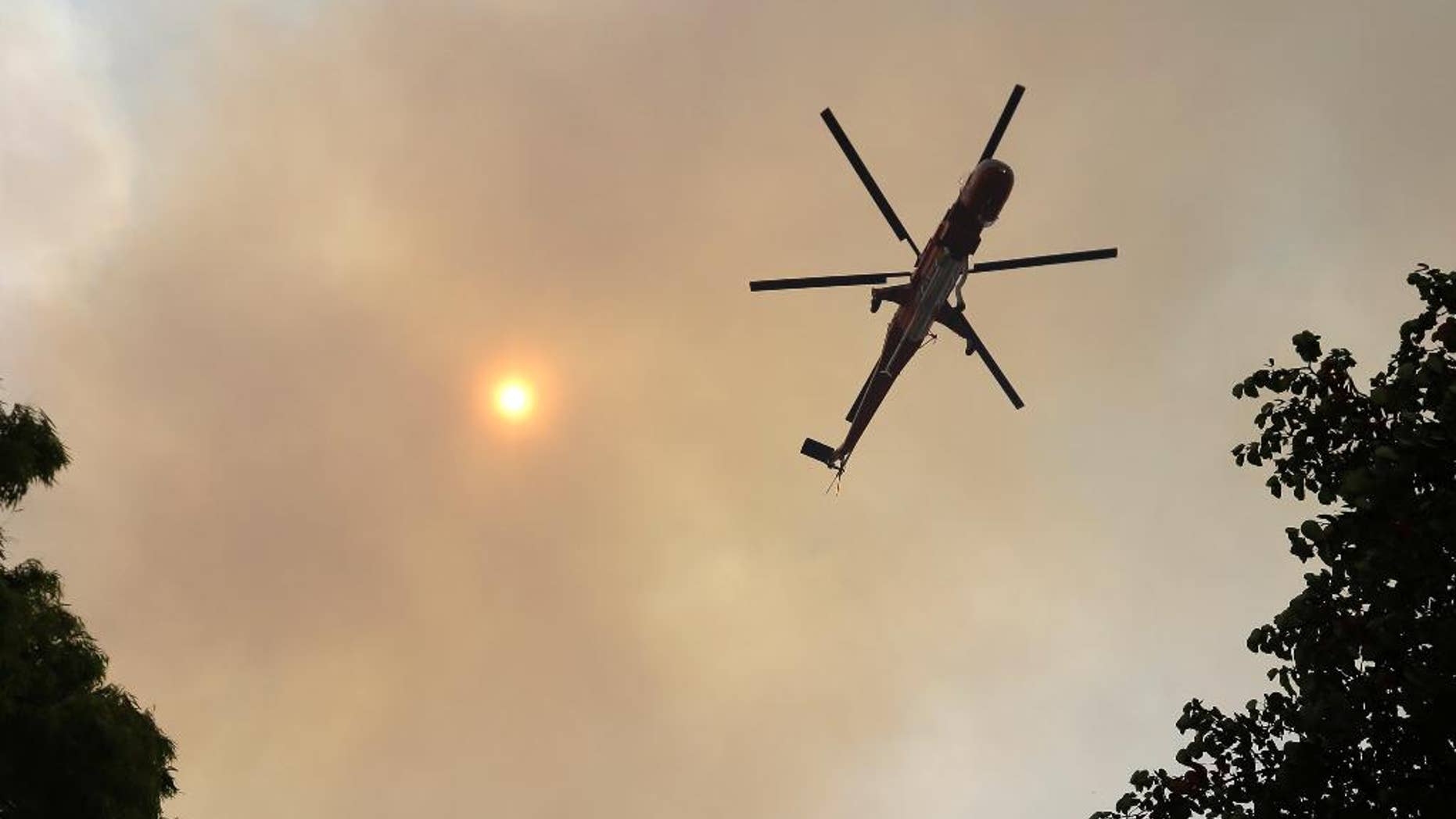 An helicopter flies over a forest at the village of Limni on the island of Evia, about 160 kilometers (100 miles) north of Athens, Monday, Aug. 1, 2016. Nearly 200 firemen, assisted by water-dropping aircraft, fire engines and volunteers, are fighting a large forest fire that has raged through the Greek island of Evia for the past three days. (AP Photo/Thanassis Stavrakis)
