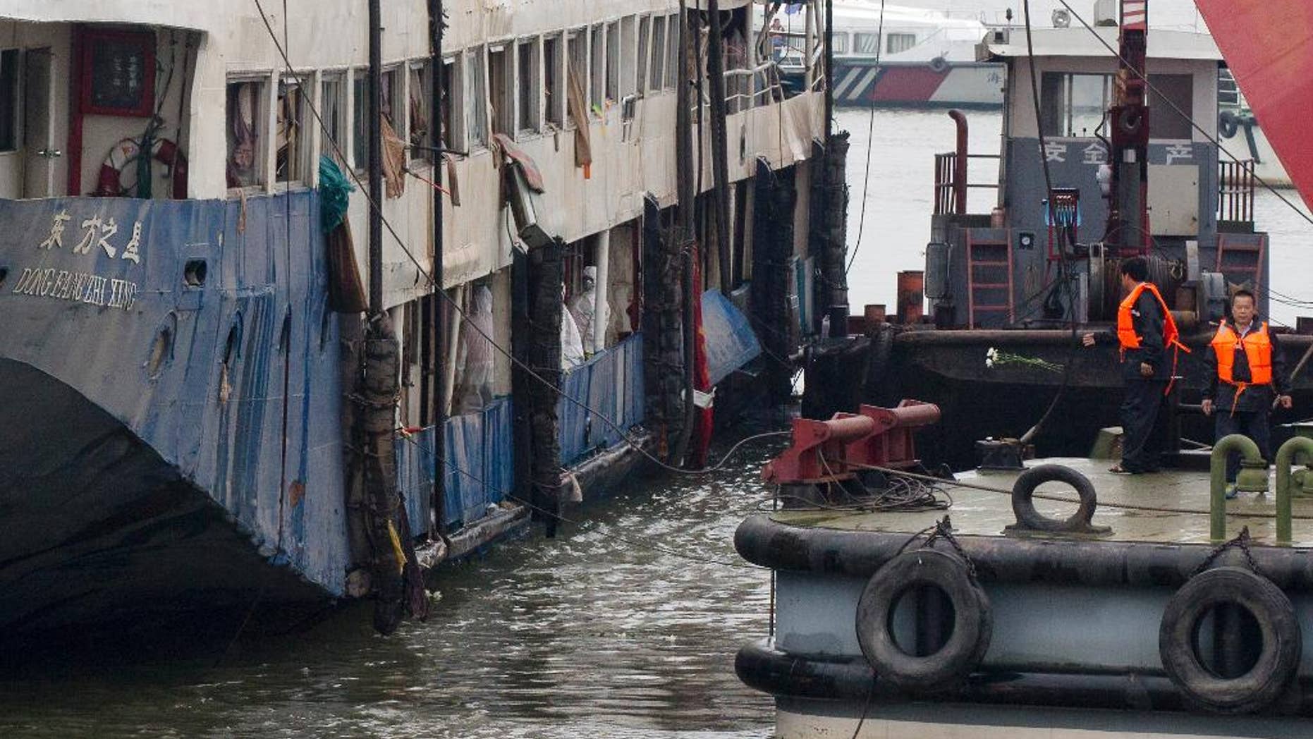 FILE - In this June 7, 2015 file photo, a Chinese rescuer, second from right, throws flowers into the Yangtze River to pay respects to the victims after a memorial service near the raised capsized ship Eastern Star in Jianli county of southern China’s Hubei province. Chinese authorities slightly revised the number of people who survived when the river cruise ship capsized this month, saying that 12 of 454 people on board lived, down by two from the previously reported number of 14, a state broadcaster said Saturday, June 13, 2015. (AP Photo/Andy Wong, File)