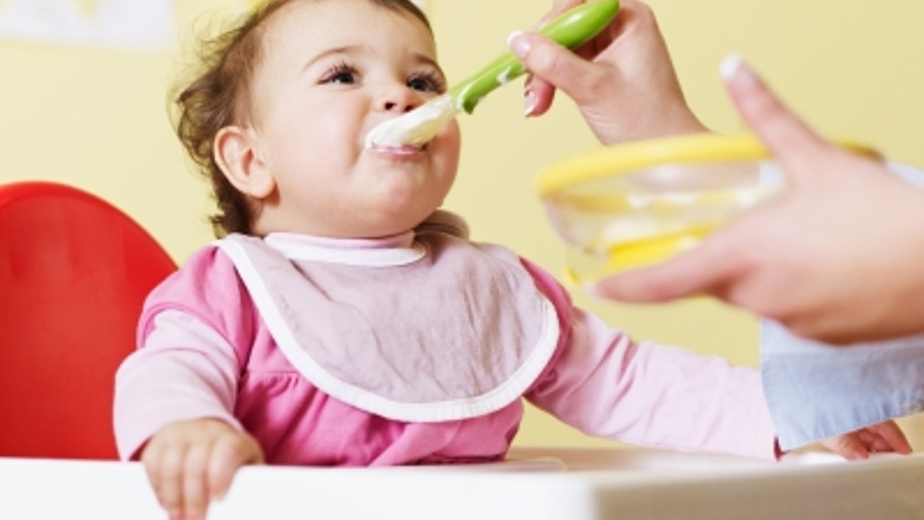 mom giving homogenized food to her daughter on high chair. Horizontal shape