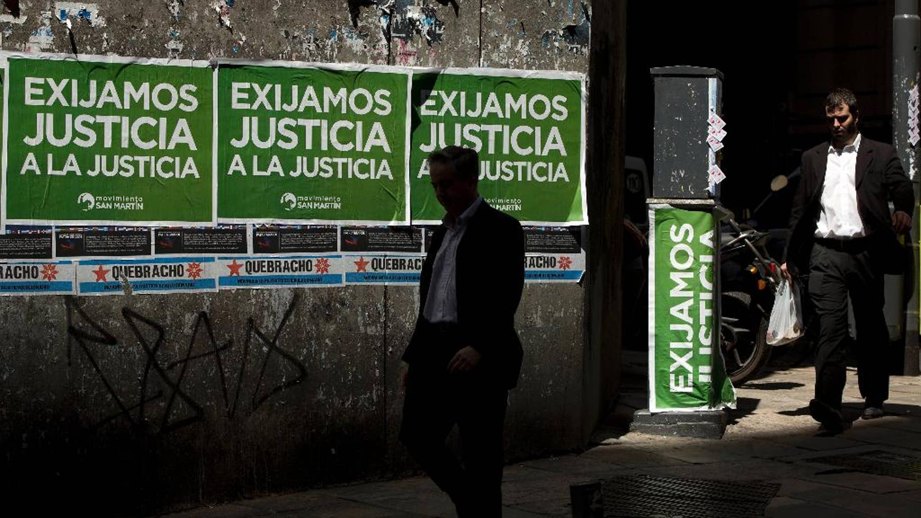 Men walk pass posters that read in Spanish "Demand justice to justice", in reference to march organized by federal prosecutors demanding justice after the death of special prosecutor Alberto Nisman almost a month ago, in Buenos Aires, Argentina, Friday, Feb. 13, 2015. Nisman accused President Cristina Fernandez, Foreign Minister Hector Timerman and others in her administration of brokering the cover-up in the bombing of a Jewish community center in exchange for favorable deals on oil and other goods from Iran. Fernandez and Timerman have strongly denied the accusations, and Iran has repeatedly denied involvement in the bombing, which killed 85 people. (AP Photo/Rodrigo Abd)
