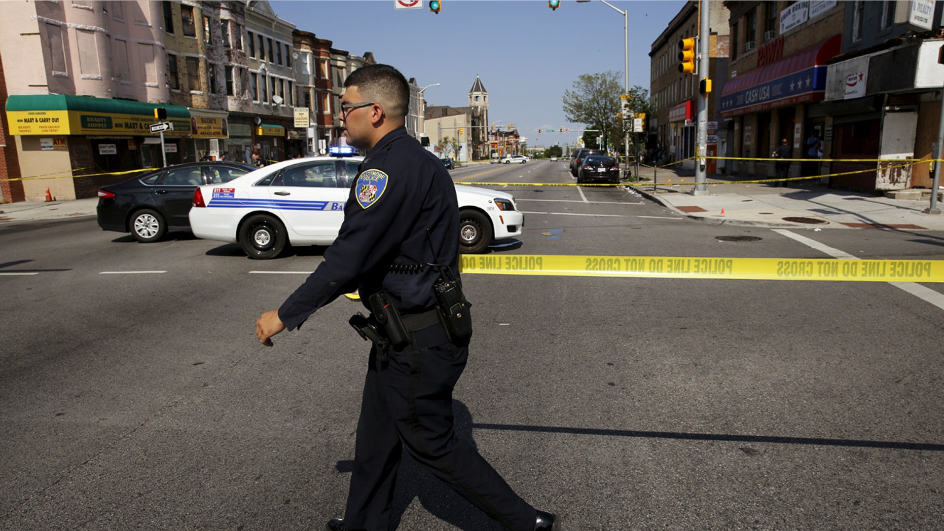 A Baltimore police officer attempts to secure a crime scene with tape at the scene of a shooting at the intersection of West North Avenue and Druid Hill Avenue in West Baltimore, Maryland.
