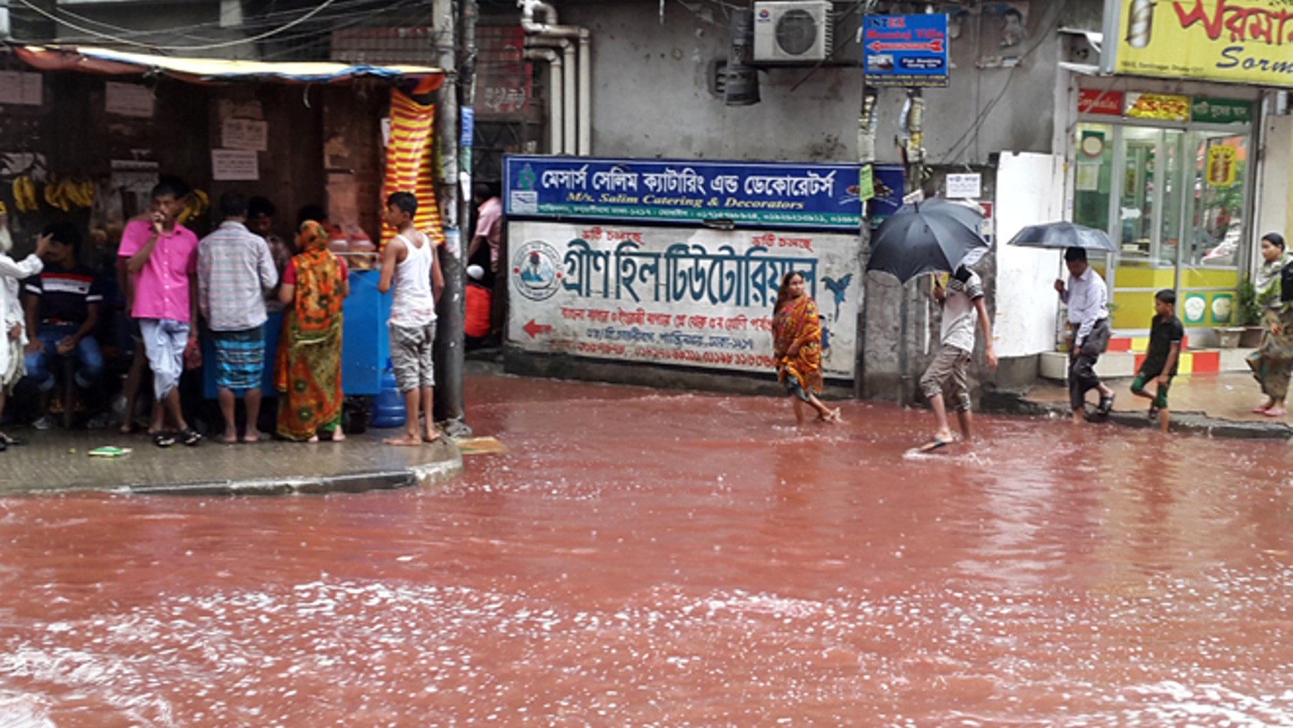 In this Tuesday, Sept. 13, 2016 photo, people wade past a road turned red after blood from sacrificial animals on Eid al-Adha mixed with water from heavy rainfall in Dhaka, Bangladesh.