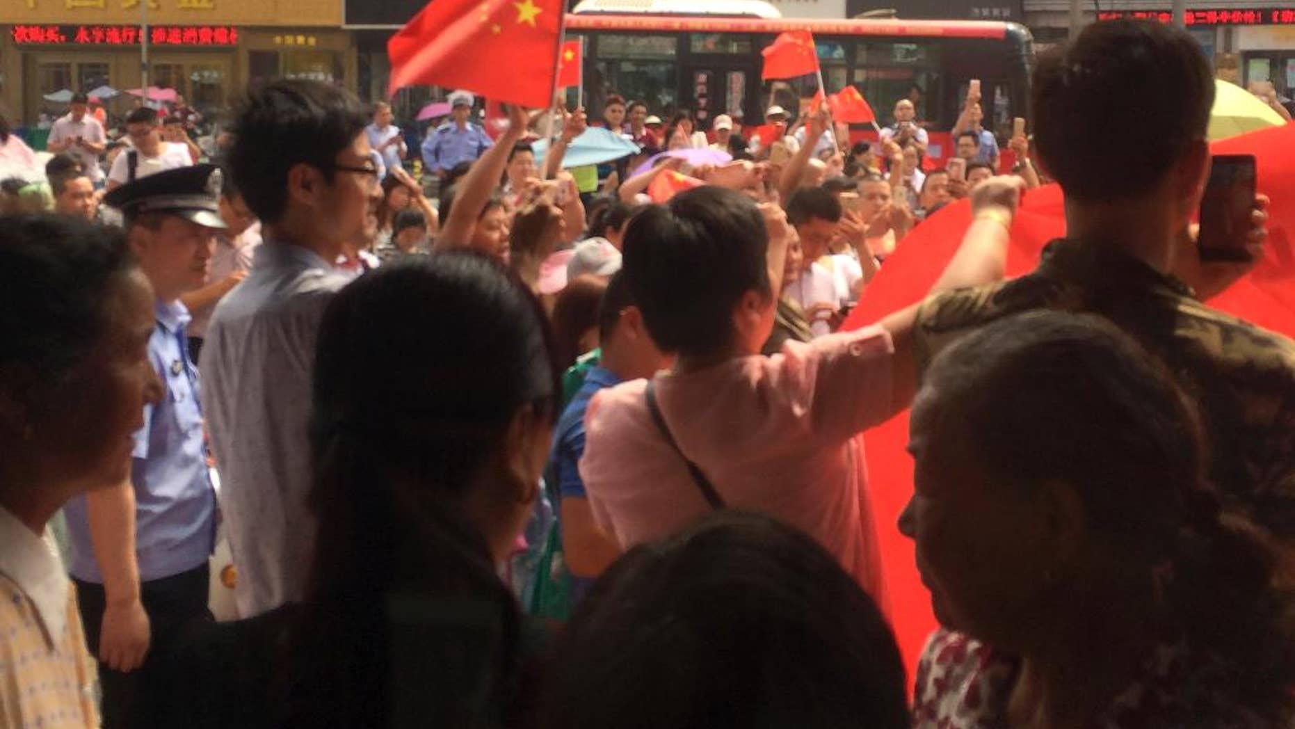 In this photo taken on Tuesday, July 19, 2016 and released by Guo Lu, policemen stand watch Chinese people carrying national flags hold a protest outside a KFC restaurant outlet in Baoying county in east China's Jiangsu province. In an apparent attempt to head off large-scale street demonstrations, Chinese state newspapers have criticized scattered protests against KFC restaurants and other U.S. targets sparked by an international tribunal's ruling that denied Beijing's claim to virtually the entire South China Sea. (Guo Lu via AP)