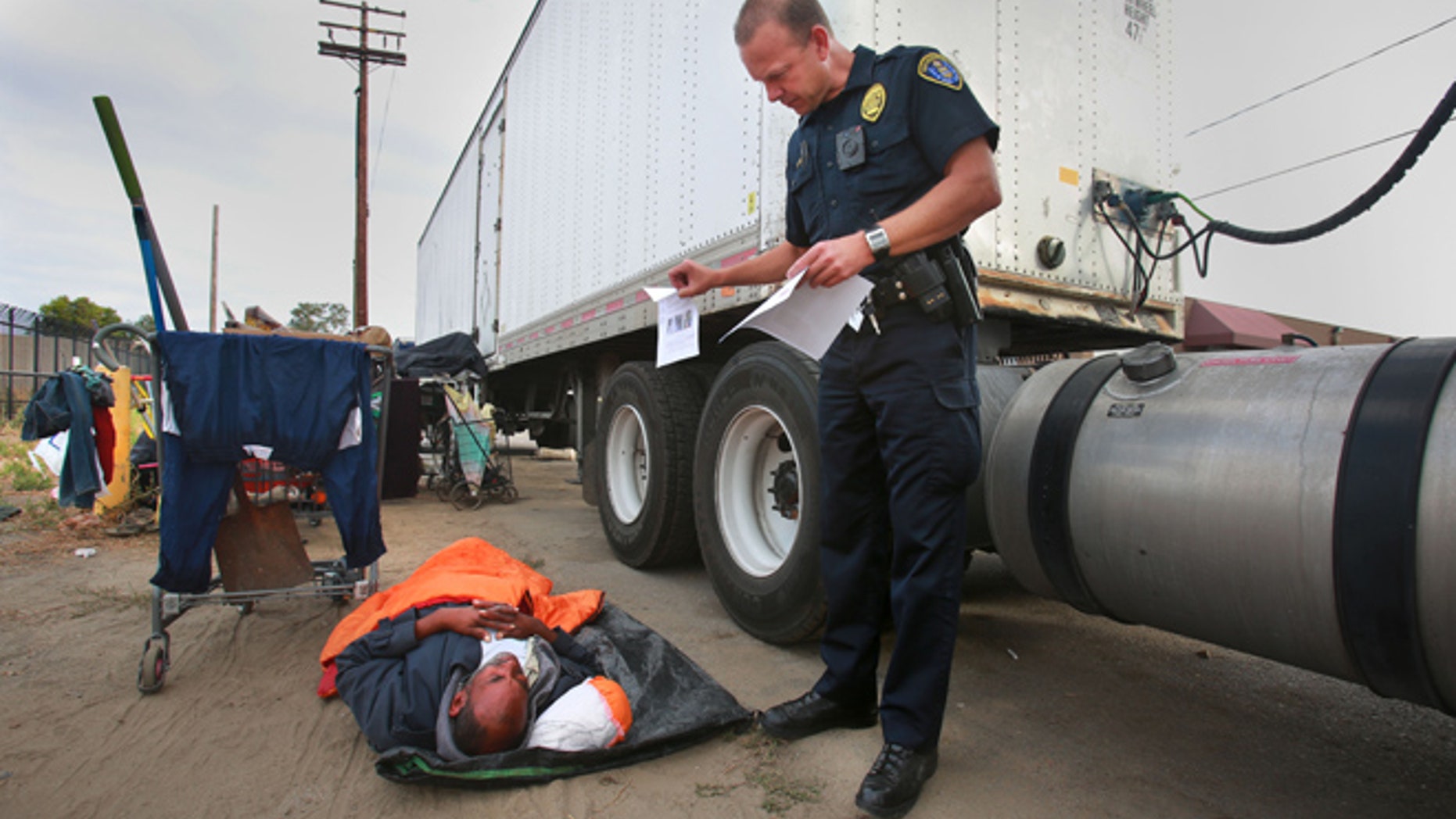 FILE - In this July 6, 2016, file photo, Ronald Mays, who rolles over to look at the flyer with pictures of a suspect in recent assaults on the homeless, as San Diego Homeless Outreach Team officer Brian Lucchesi canvasses several areas in the Midway and Sports Arena Blvd. area stopping to talk with people in San Diego. (Peggy Peattie/U-T San Diego via AP, File)
