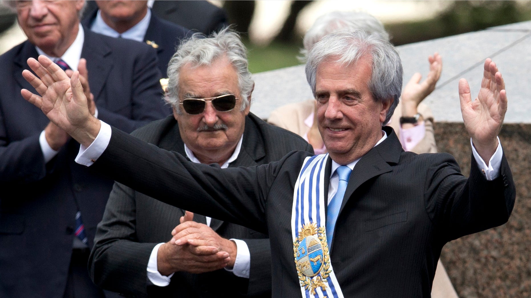 Uruguay's new President Tabare Vazquez waves to the crowd wearing the presidential sash as outgoing President Jose Mujica looks on, behind center, during his inauguration ceremony at Independence Plaza in Montevideo, Uruguay, Sunday, March 1, 2015. (AP Photo/Natacha Pisarenko)