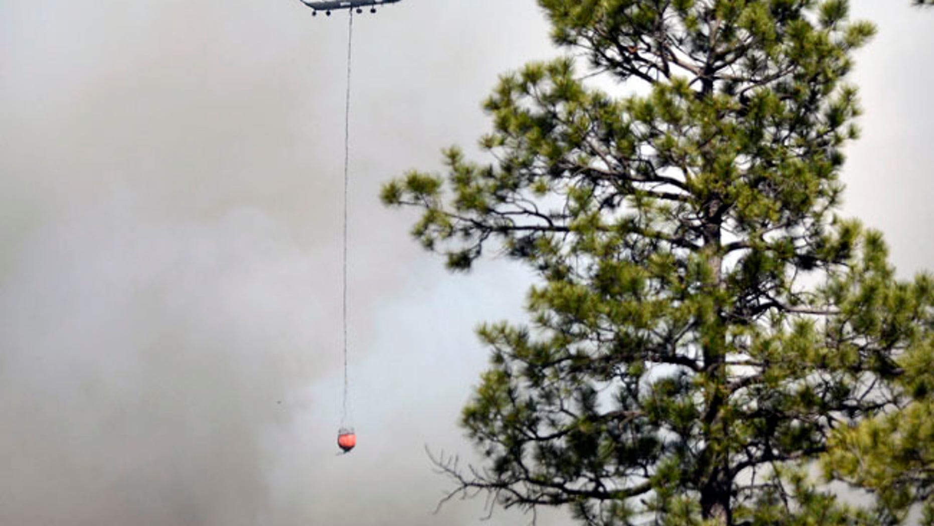 A Chinook Helicopter with a bucket heads towards the structures in the community of Ruby Hole, New Mexico. Thursday June 15, 2017. (Jim Thompson/The Albuquerque Journal via AP)