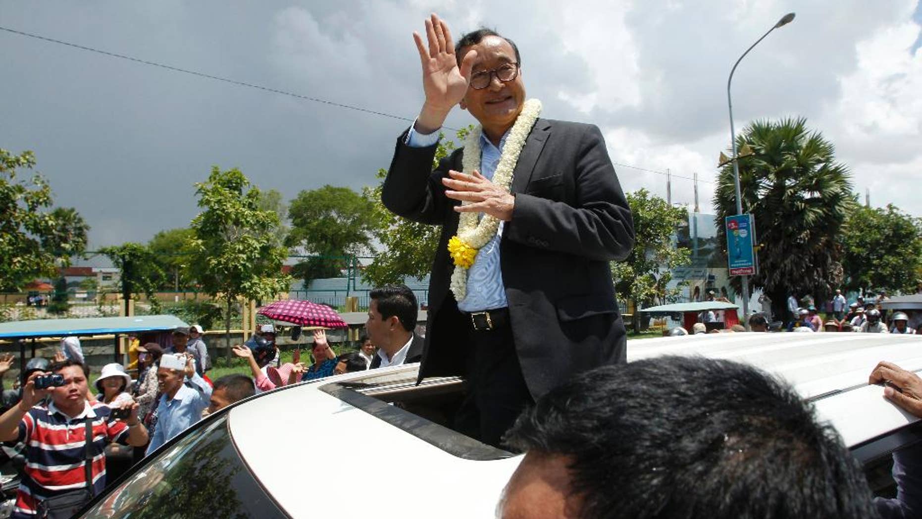 FILE - In this Aug. 16, 2015 file photo, Sam Rainsy, leader of the opposition Cambodia National Rescue Party (CNRP), waves from a car upon his arrival at Phnom Penh International Airport in Phnom Penh, Cambodia as hundreds of cheering supporters greeted him on his return from a trip abroad. The head of Cambodia's opposition party has announced his resignation from the group after the country's long-serving prime minister announced plans for a law that could lead to the party's dissolution. Rainsy announced his resignation Saturday, Feb. 11, 2017 in a letter to his Cambodia National Rescue Party.(AP Photo/Heng Sinith, File)