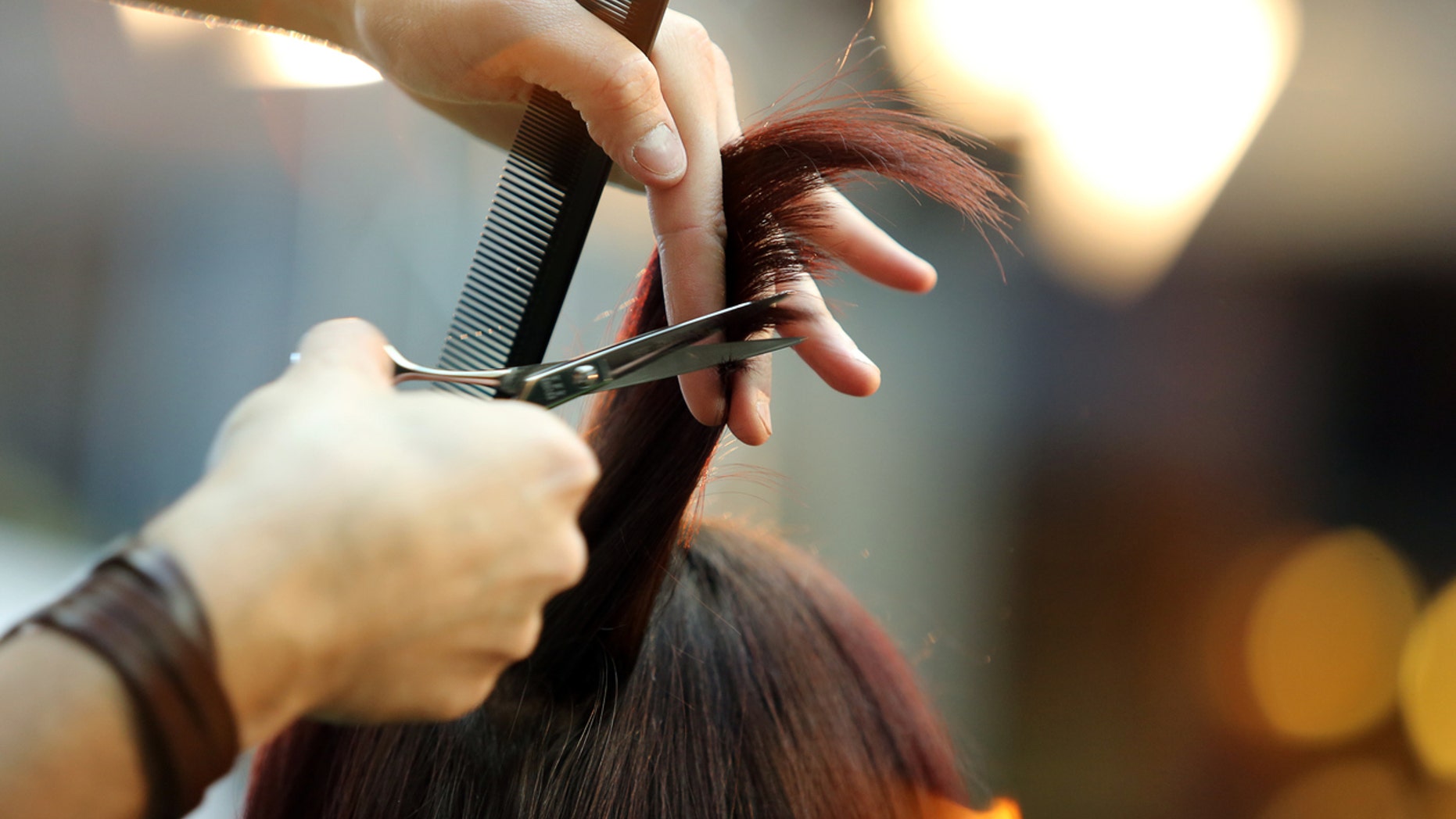 Hairdresser trimming blond hair with scissors