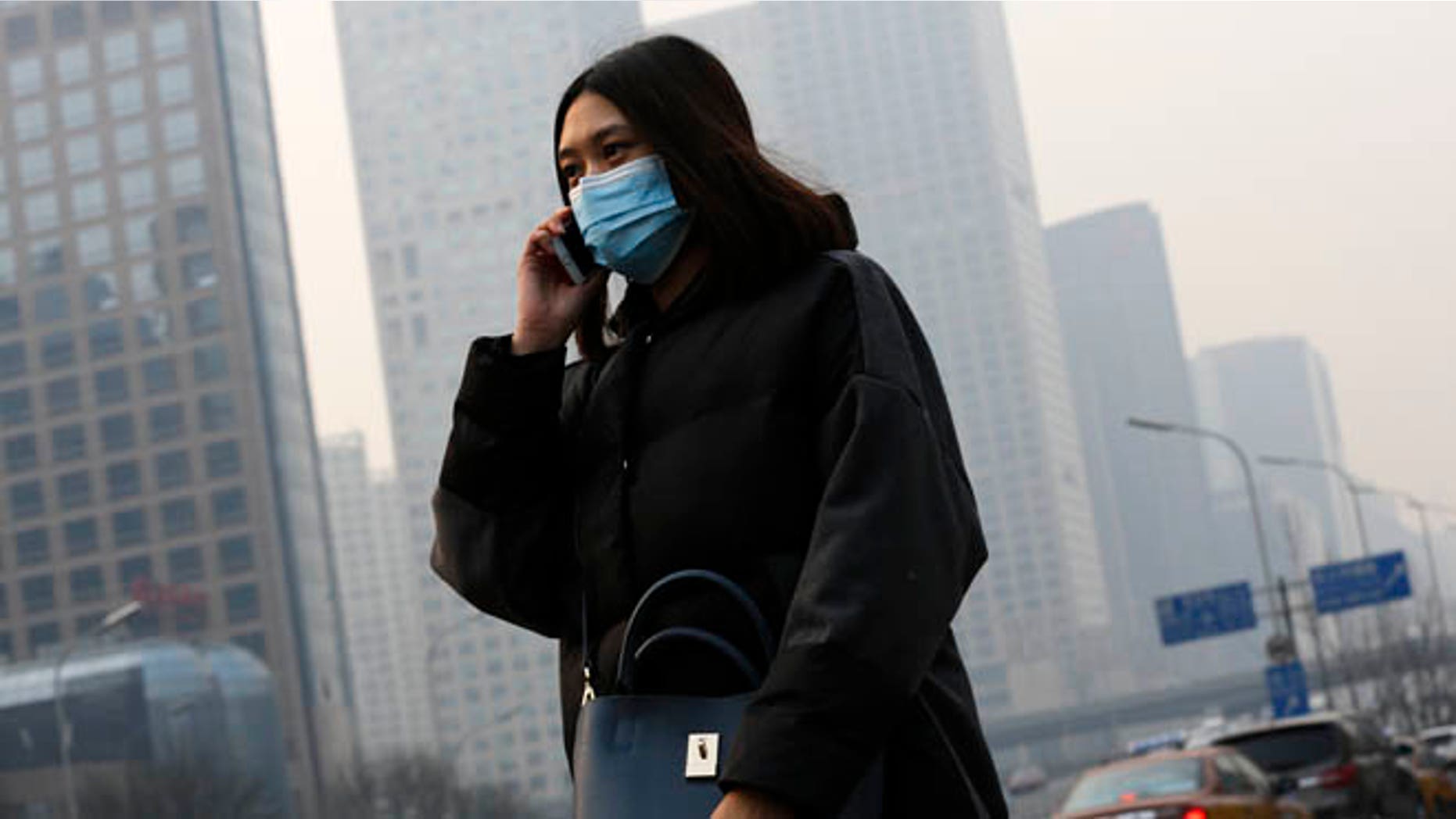 Dec. 7, 2015: A woman wearing a mask to protect herself from pollutants walks past office buildings shrouded with pollution haze in Beijing. Smog shrouded the capital city Monday after authorities in Beijing issued an orange alert on Saturday.