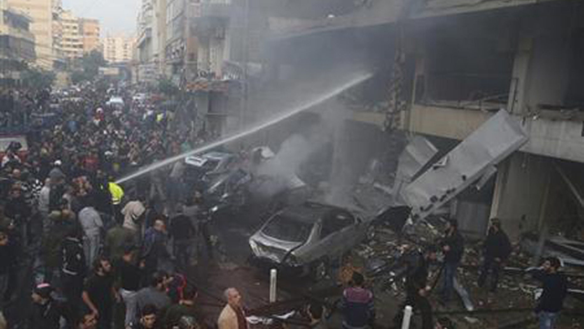 People gather as firefighters attempt to extinguish a fire at the site of an explosion in Beirut's southern suburbs, Jan. 2, 2014. (Reuters)